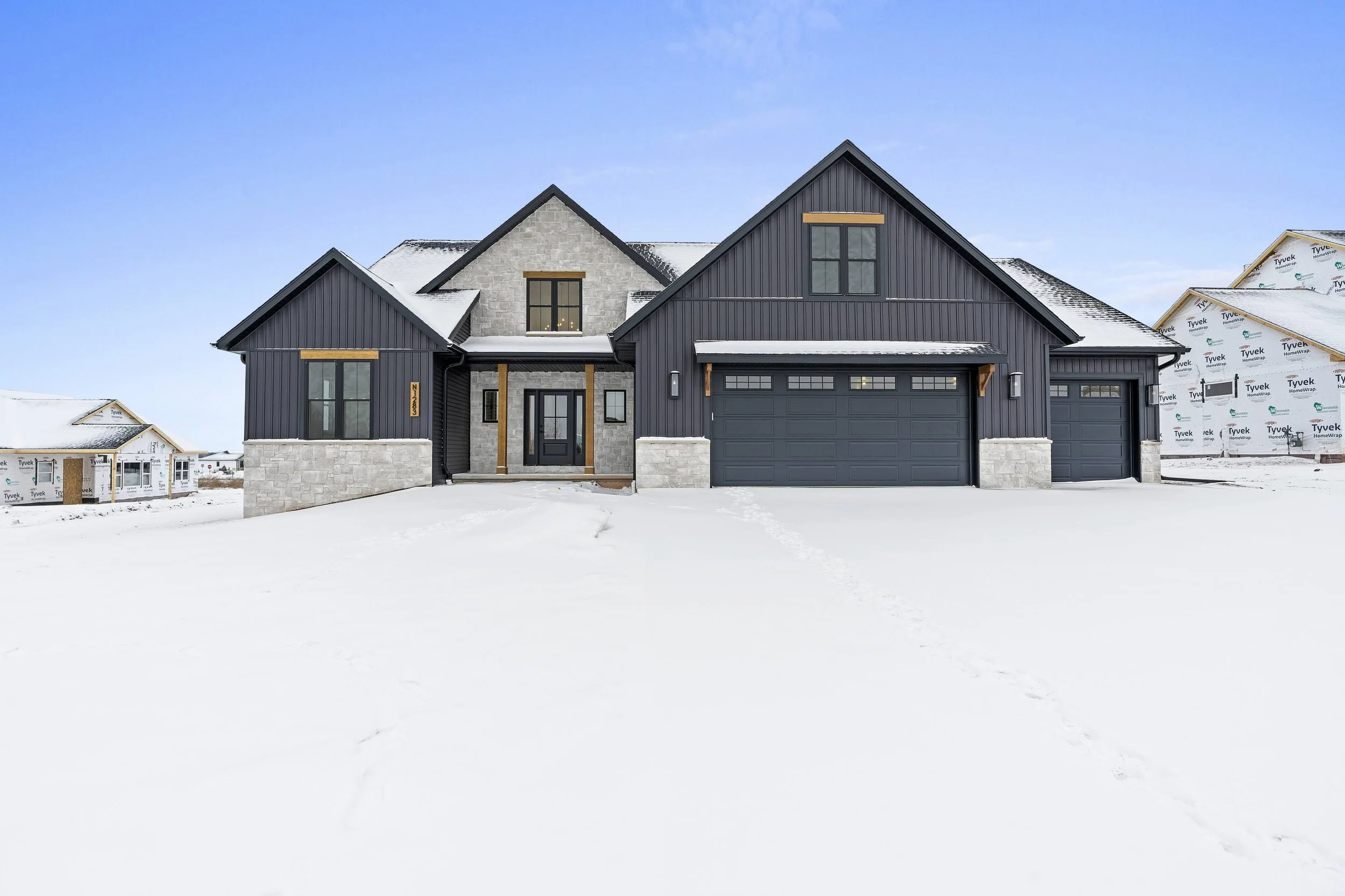 New modern house with black siding and stone accents, snow-covered yard, and clear blue sky.