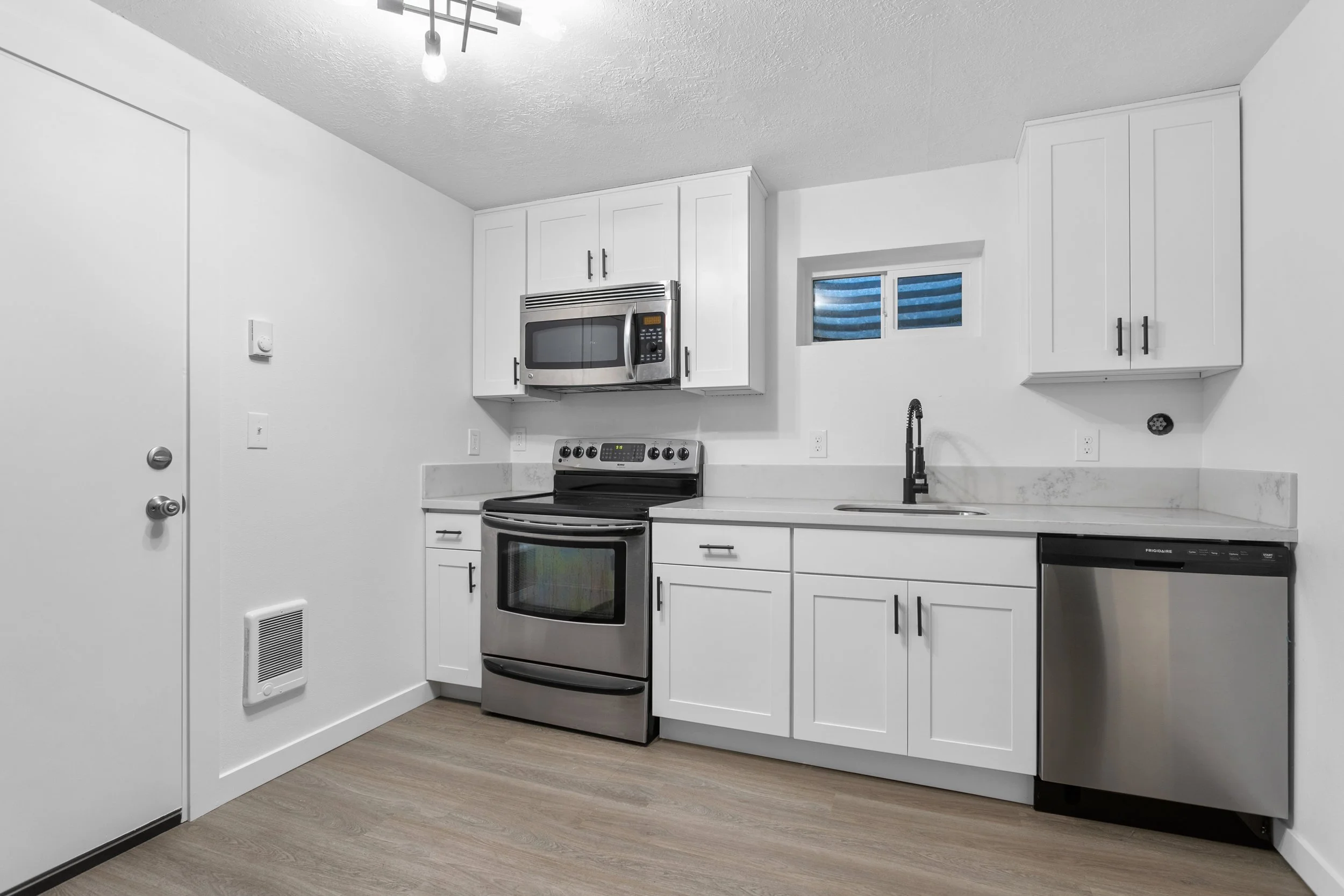Modern kitchen with white cabinets, stainless steel stove and microwave, black faucet, small window, and a dishwasher.