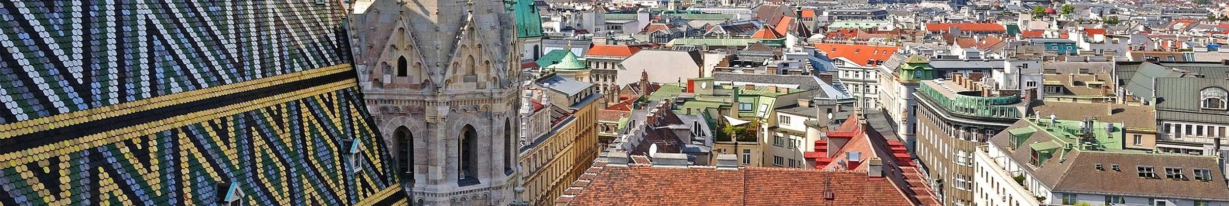 Aerial view of a European city with colorful rooftops and historic buildings, including a church tower with a pointed spire.