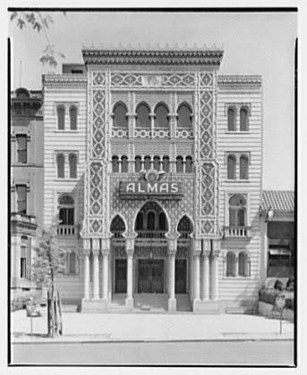 Front view of a three-story building with intricate architectural details and a sign reading 'ALMAS' above the entrance.