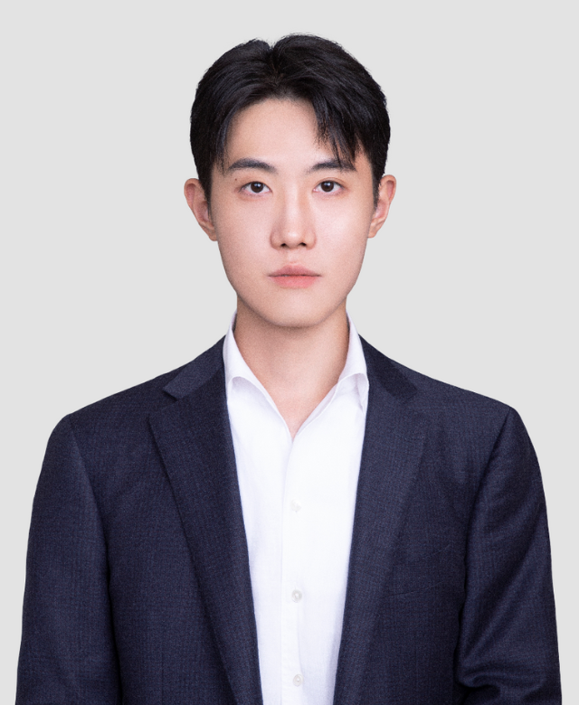 Portrait of a young Asian man in a dark blazer and white shirt against a plain gray background.