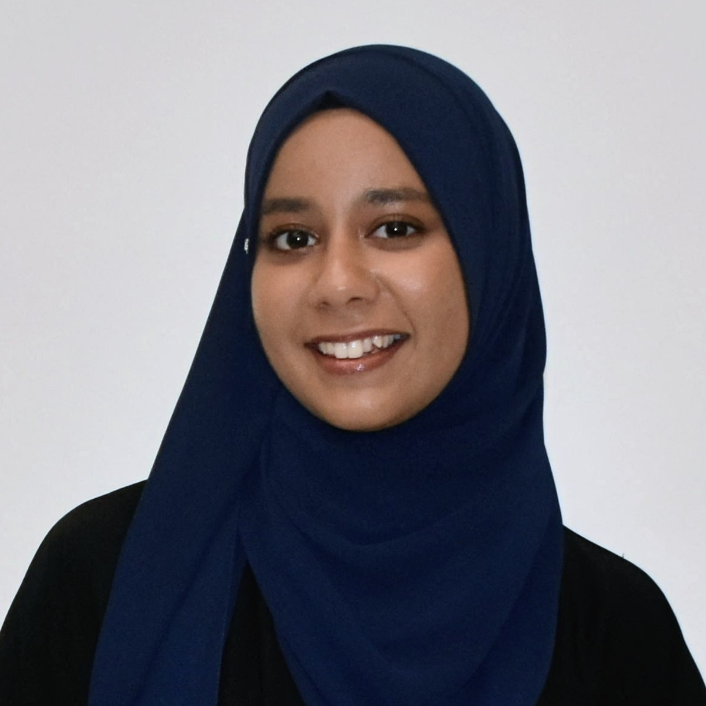 Portrait of a woman wearing a dark blue hijab and black top, smiling against a plain white background.