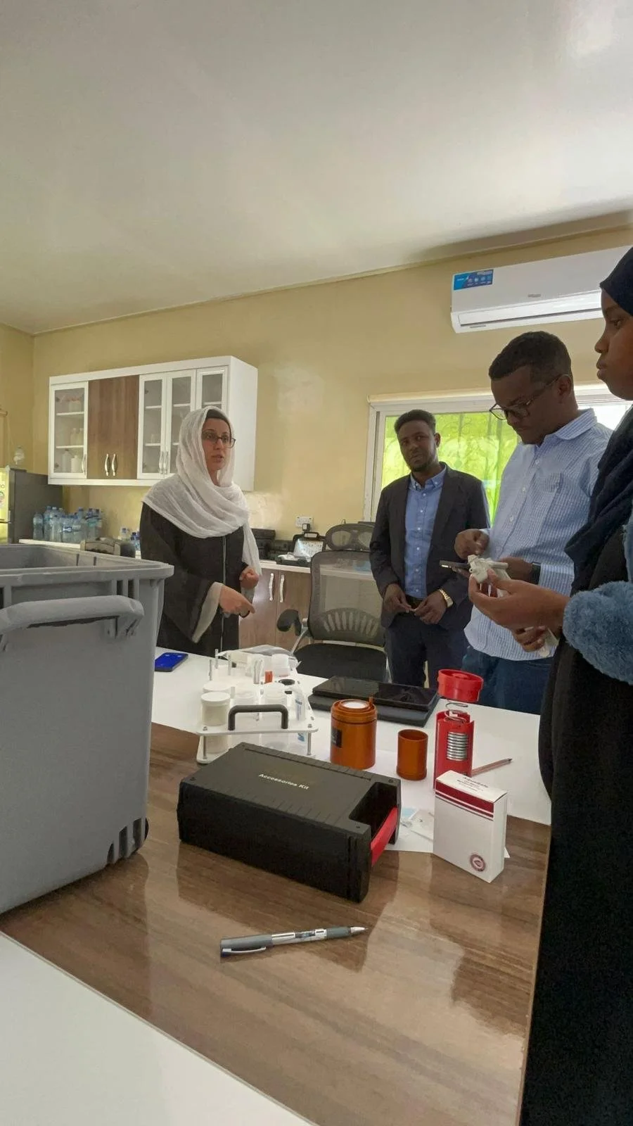 Group of four people in a laboratory or research room with scientific equipment and supplies on a table.