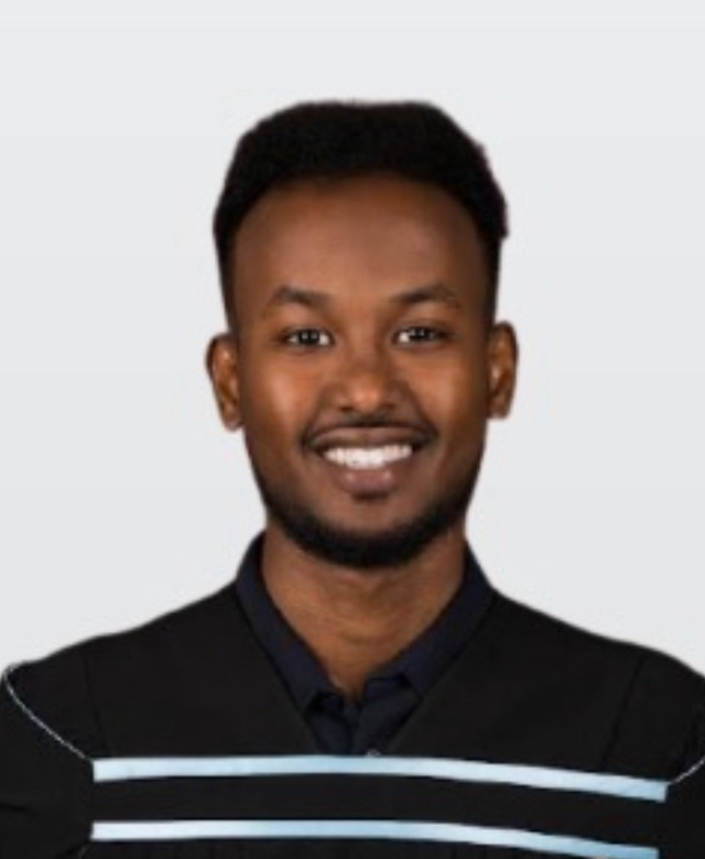 Smiling young man in a black sweater with light blue and white horizontal stripes against light gray background.