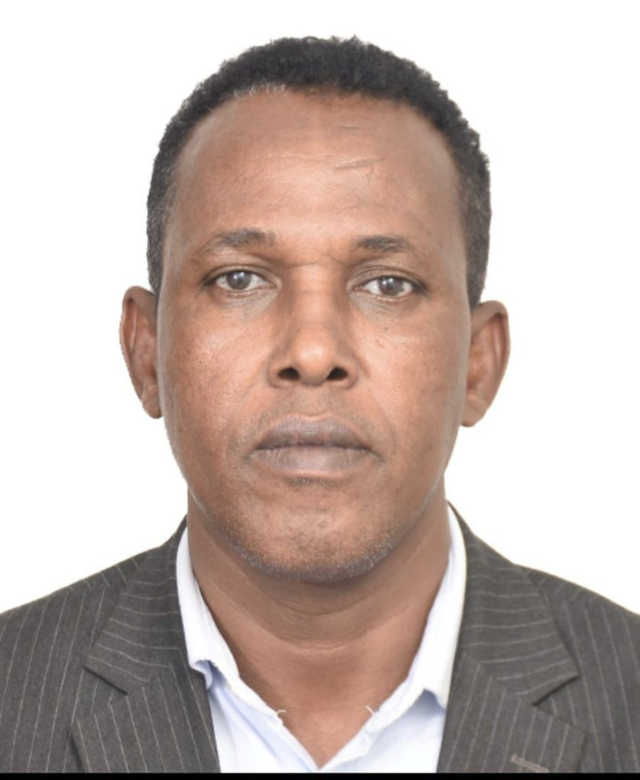 Portrait of a man wearing a black pinstripe suit and white shirt, posing against a plain white background.
