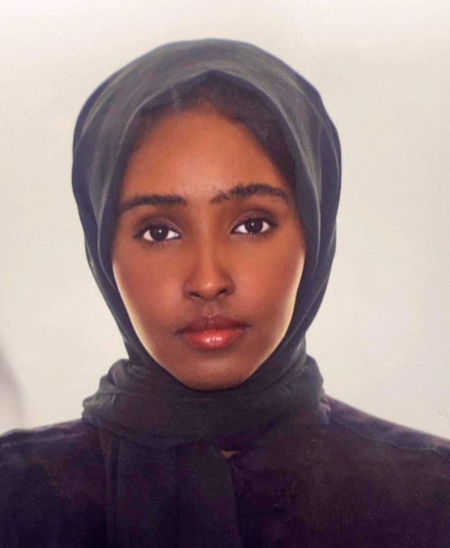 A young woman wearing a dark hijab, looking directly at the camera with a neutral expression.