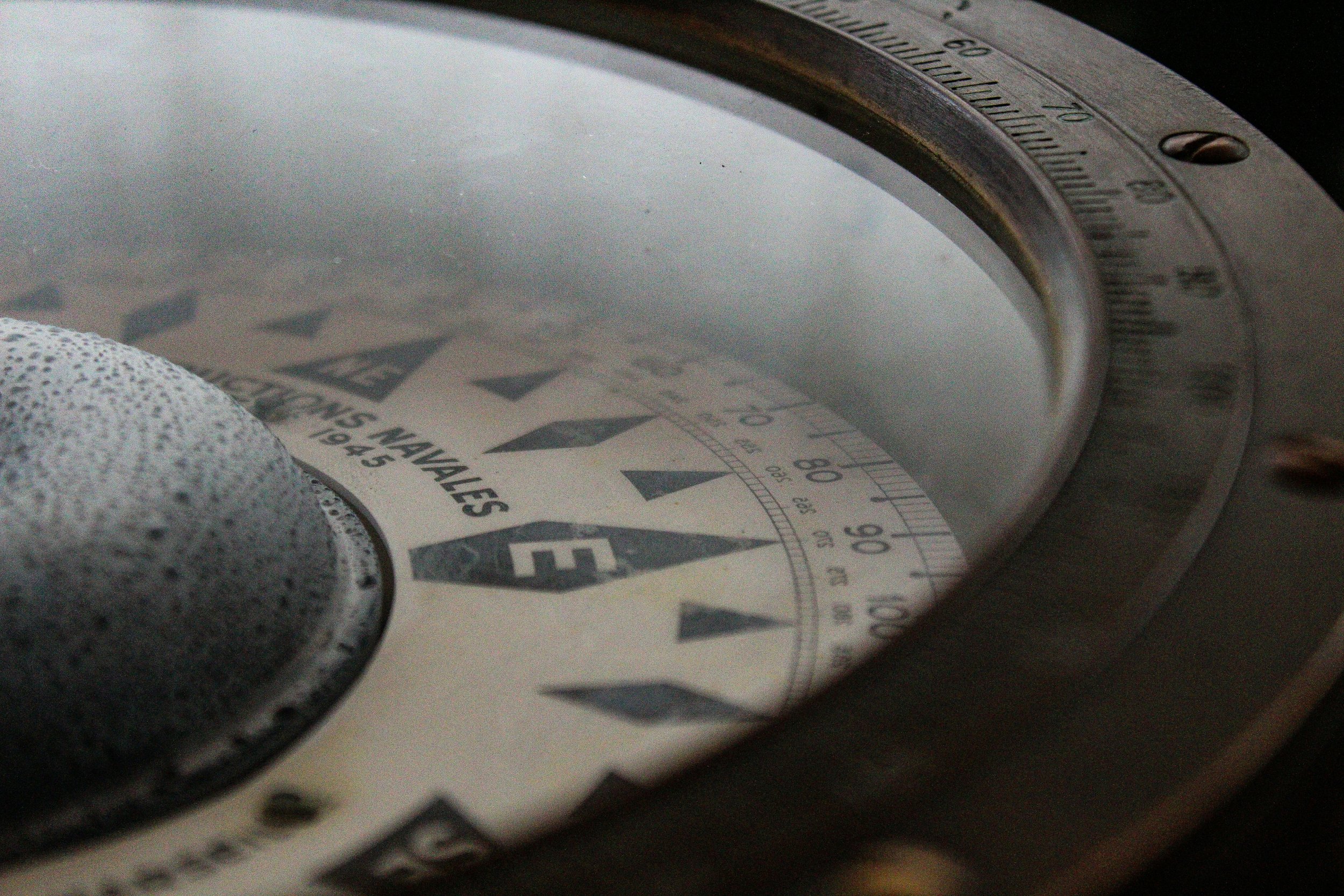 A close-up view of a vintage compass with a magnified glass showing the needle and directional markings, placed on a surface.