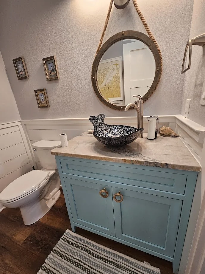 Bathroom with a white toilet, a blue vanity with a marble countertop, a decorative black sink, a mirror, and framed pictures on the wall.