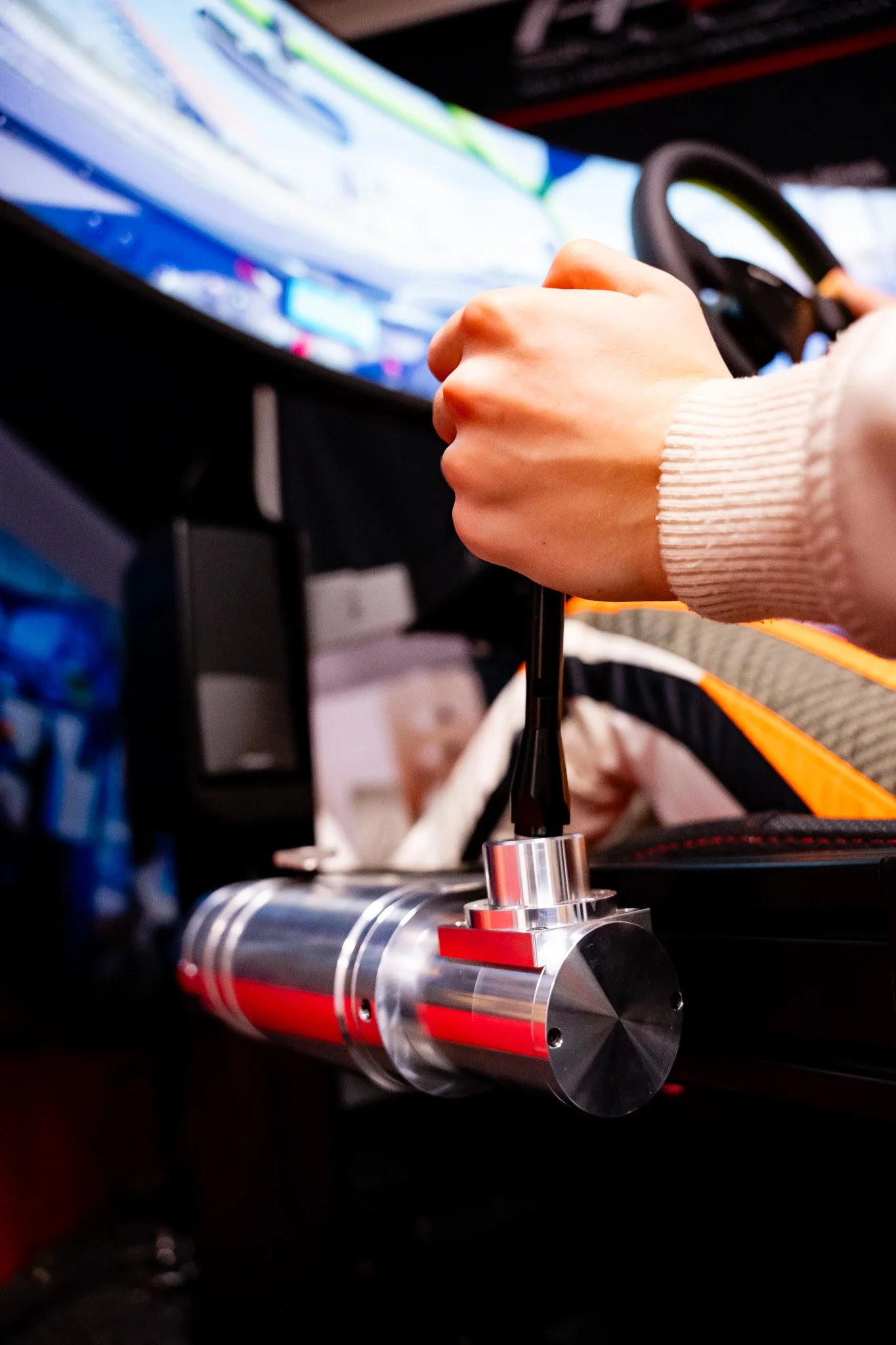 Person using a racing simulator gear shifter with a monitor displaying a racing game in the background.