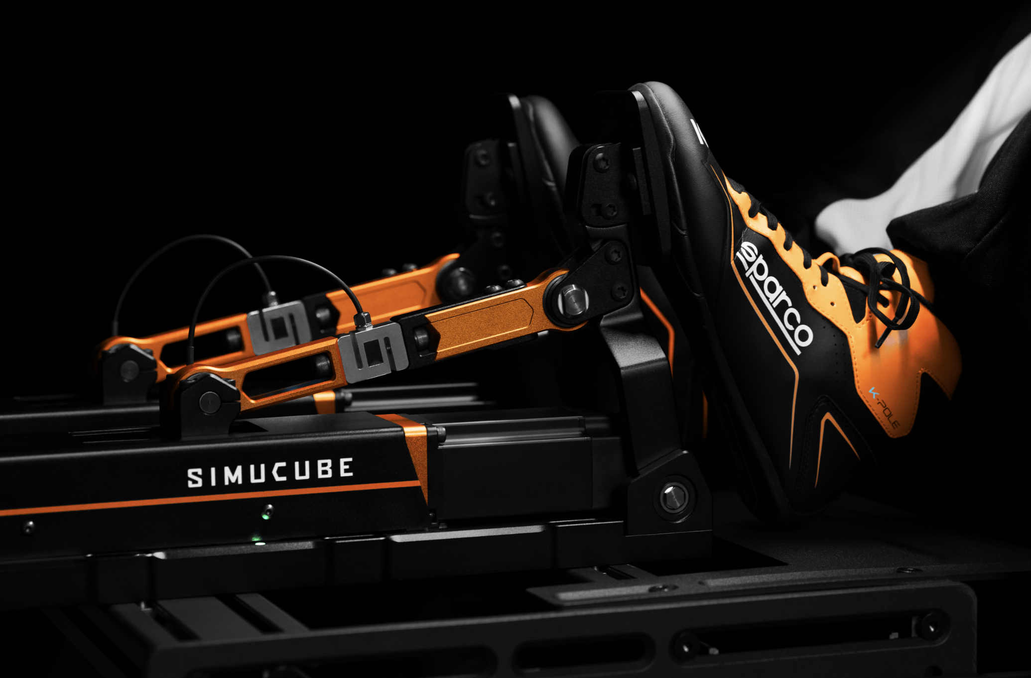Racing simulation pedals with Simucube branding and an orange Sparco racing shoe.