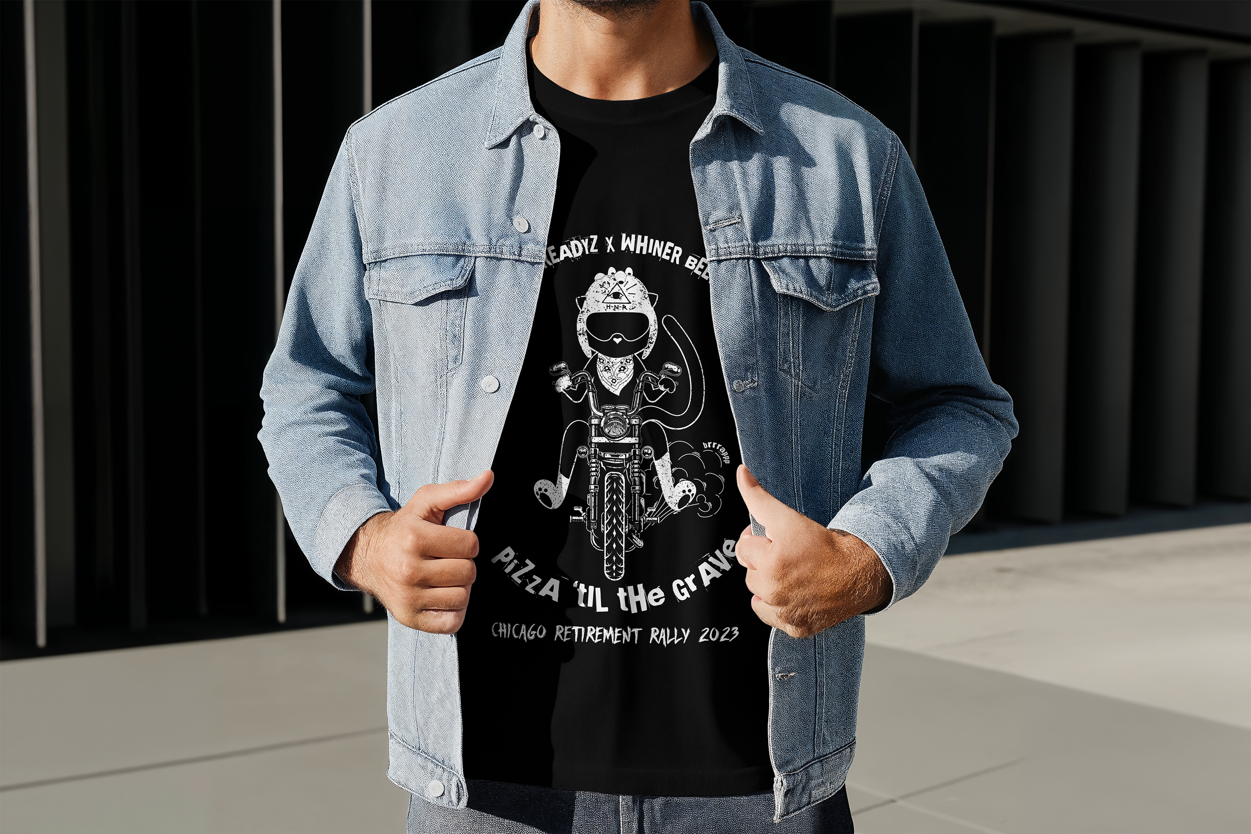 Person wearing a light blue denim jacket over a black graphic T-shirt with a cartoon character riding a motorcycle, with text reading "Pizza 'Til the Grave" and "Chicago Retirement Rally 2023".