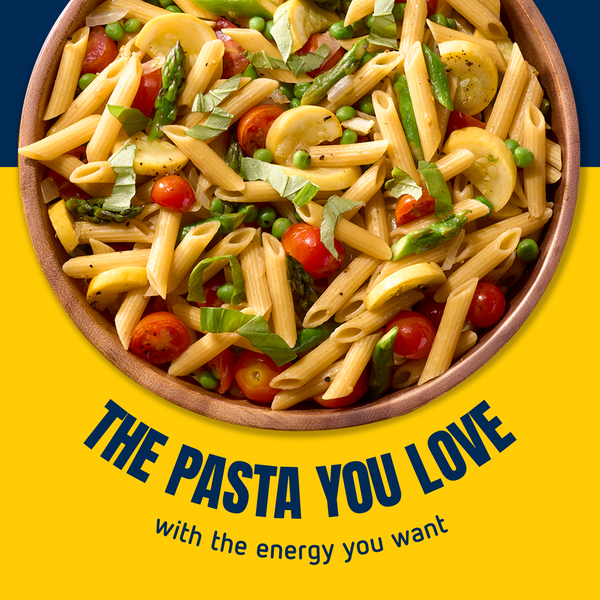 Bowl of pasta with cherry tomatoes, green peas, asparagus, and chopped basil, on a yellow background with the text "The Pasta You Love with the energy you want."