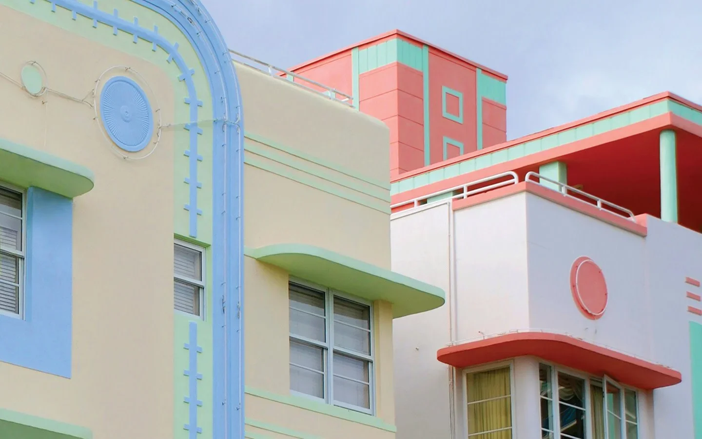 Colorful pastel-colored apartment building with geometric architectural details and round window, under a cloudy sky.