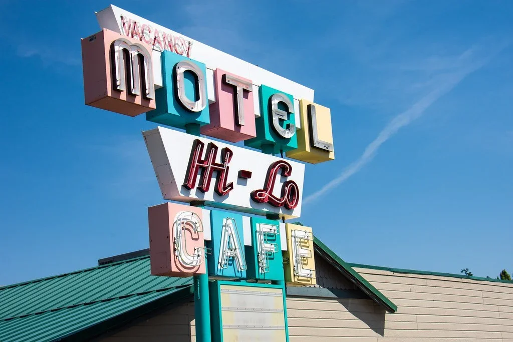 Colorful vintage motel sign on a pole with the words 'MOTEL', 'H-LQ', and 'CAFE' against a blue sky.