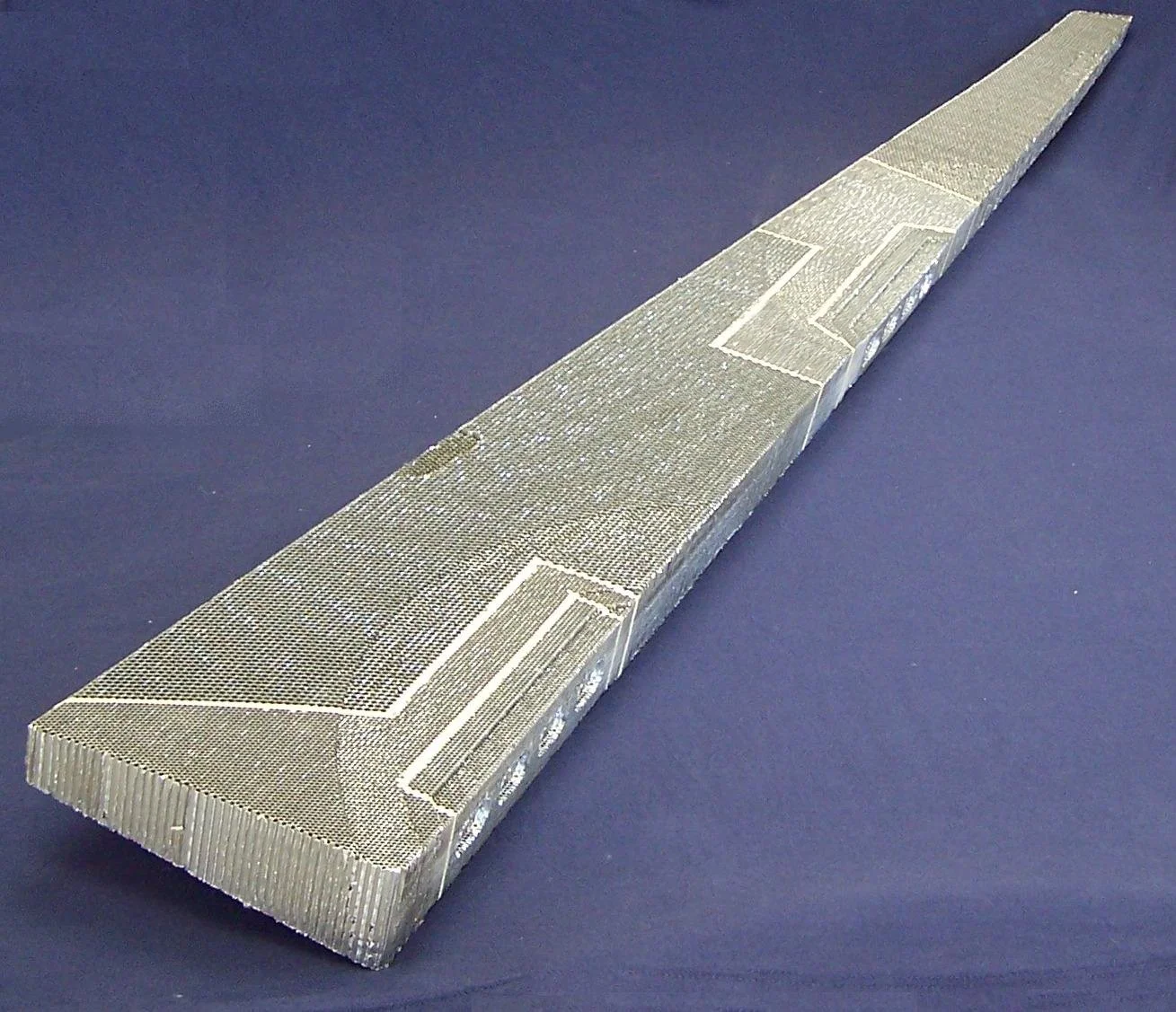 Close-up of three metallic razor blades, with one blade mainly visible and slightly curved, on a dark blue background.