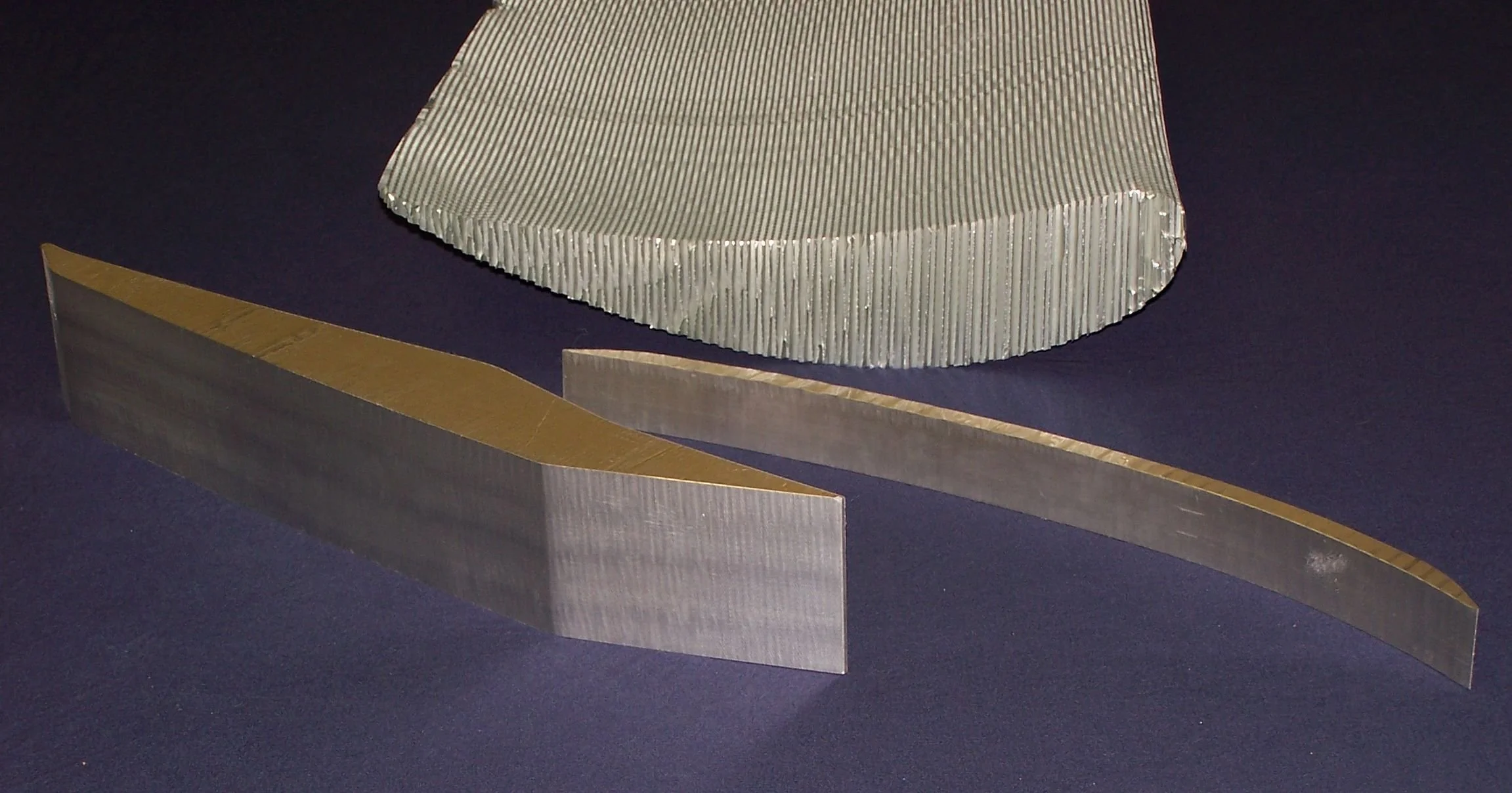 Three metallic machine parts with textured and smooth surfaces placed on a dark background.