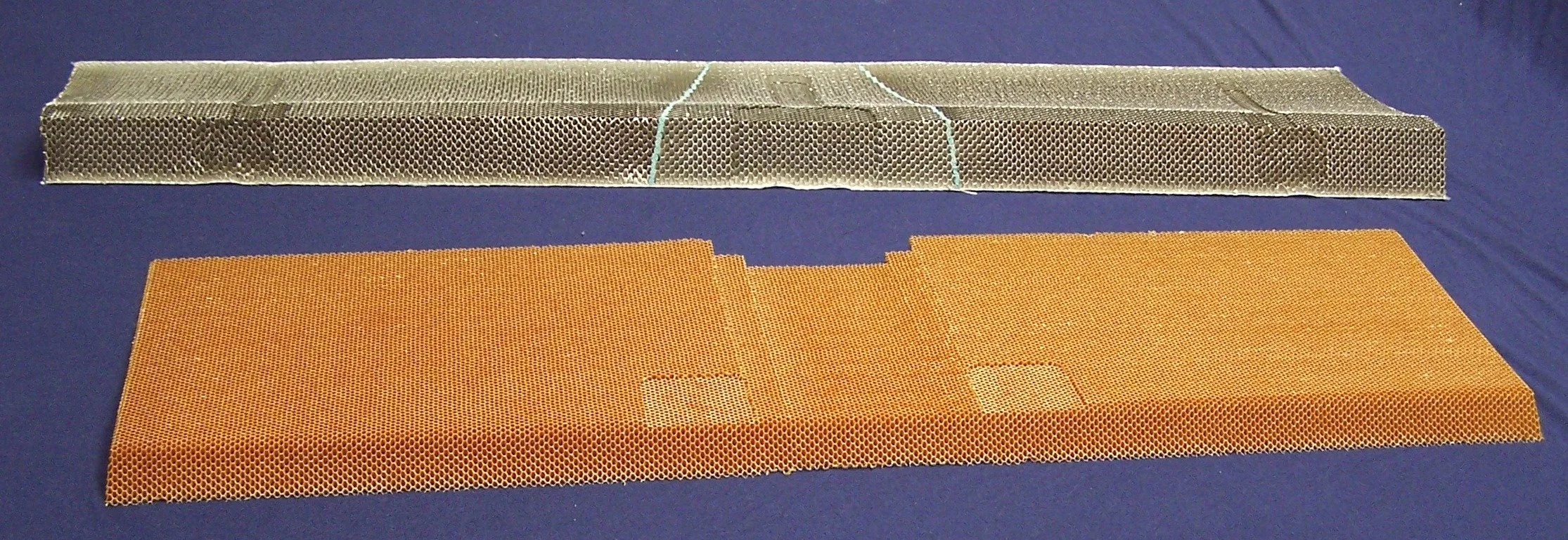 Two pieces of honeycomb mesh in different colors, one gray and one orange, laid flat on a blue surface.