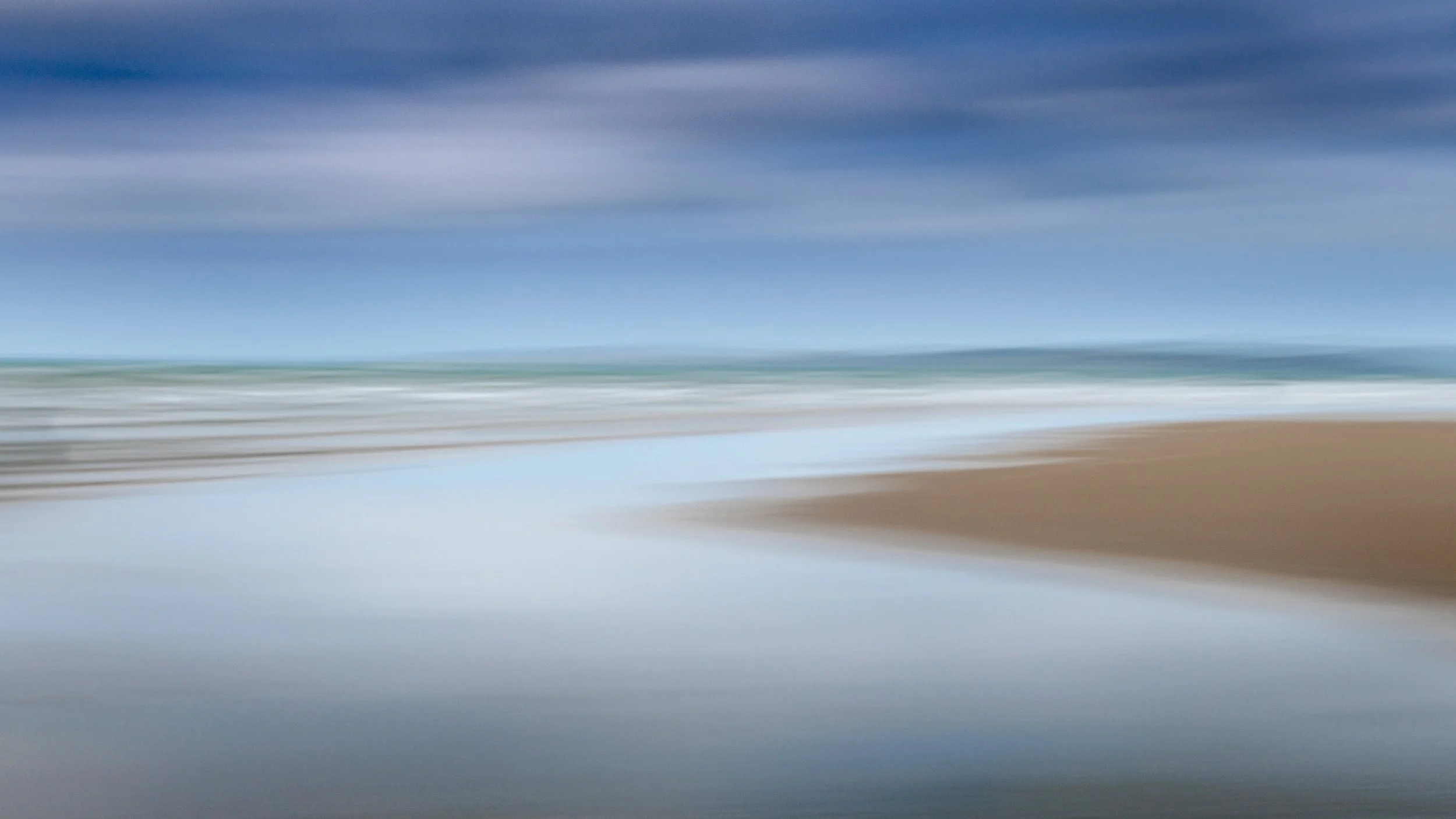 Soft blurred beach view in Orewa with sand and gentle waves.