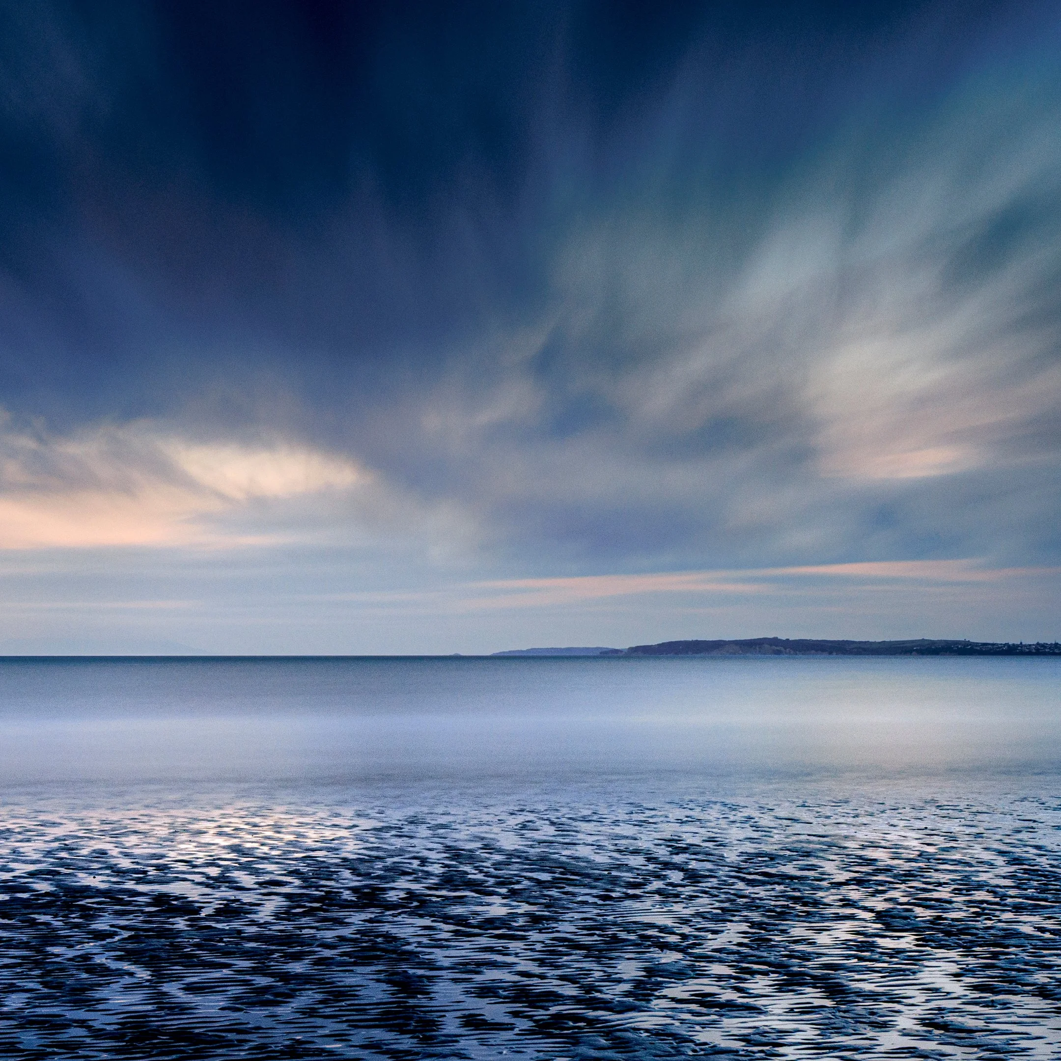 Calm ocean view in Orewa, New Zealand under soft cloudy skies.