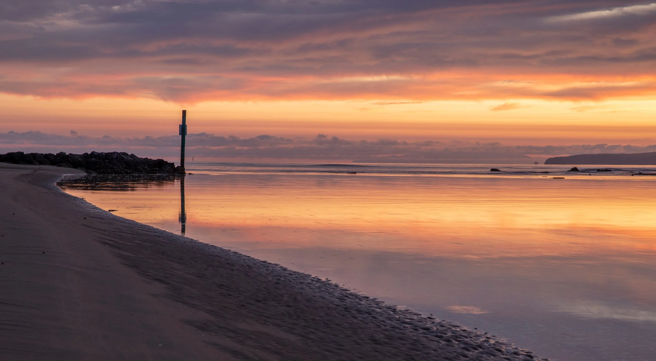 Sunset over Orewa Beach with colorful sky and reflective water.