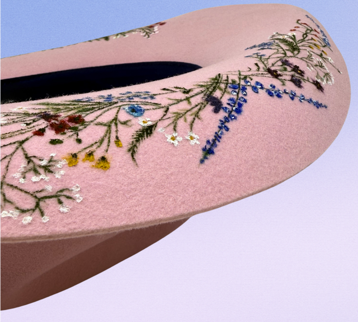 A pink felt hat decorated with painted wildflowers and green stems.