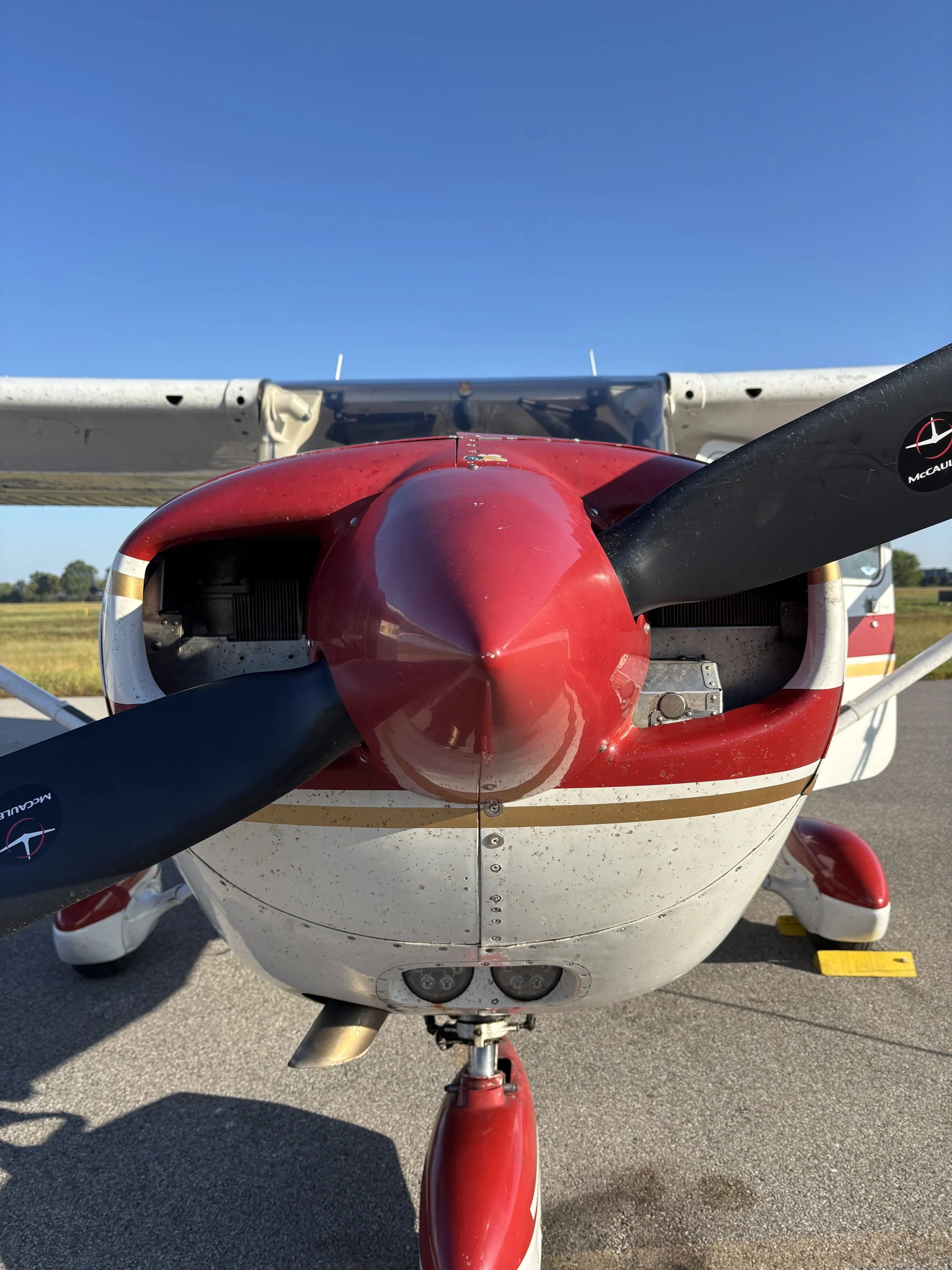 Front view of a small red and white airplane with a black propeller on a runway under a clear blue sky.