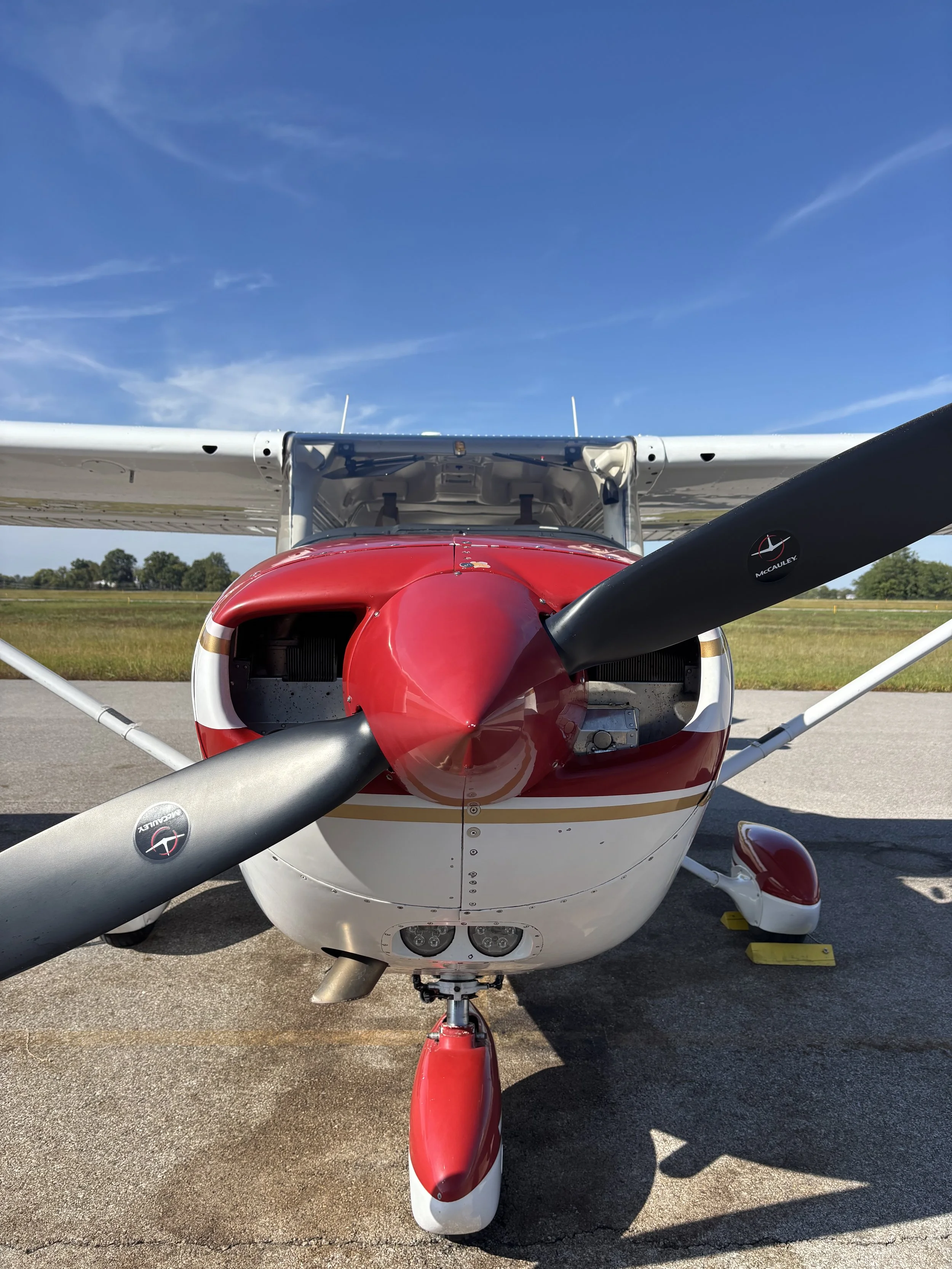 Front view of a small aircraft on the tarmac with a blue sky and grassy field in the background.