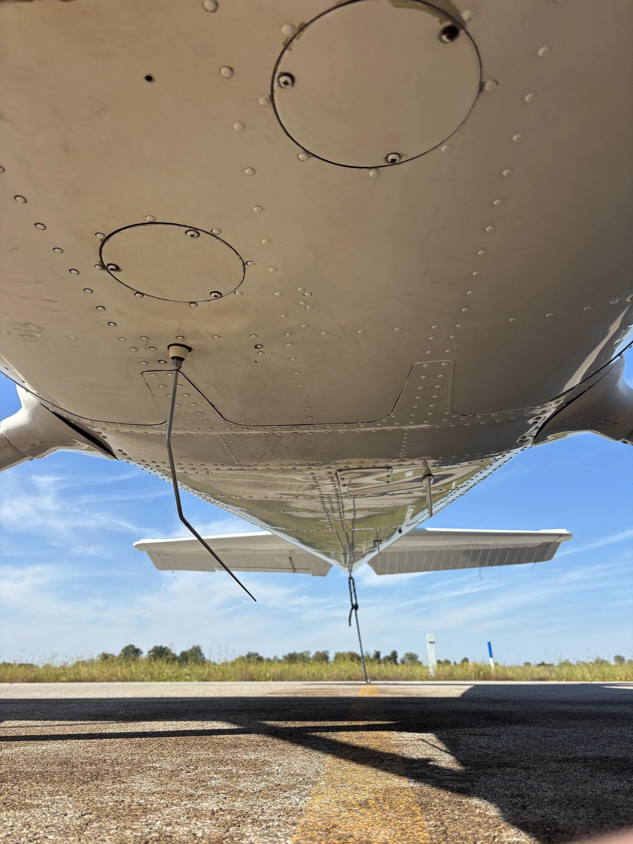 Underneath view of a small airplane on a runway showing the landing gear, part of the wing, and the sky.