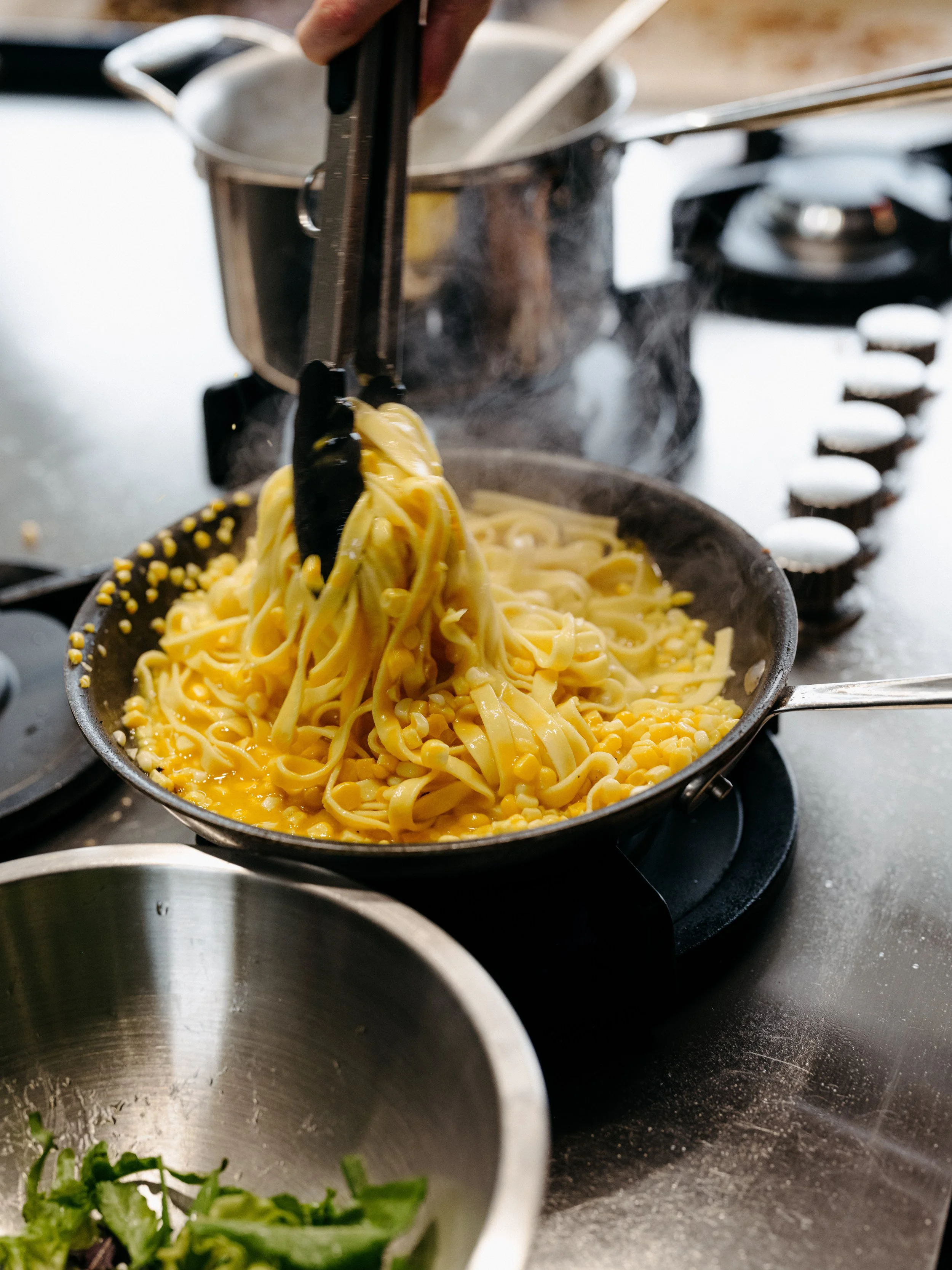 Cooking pasta with corn in a black skillet on a stovetop.