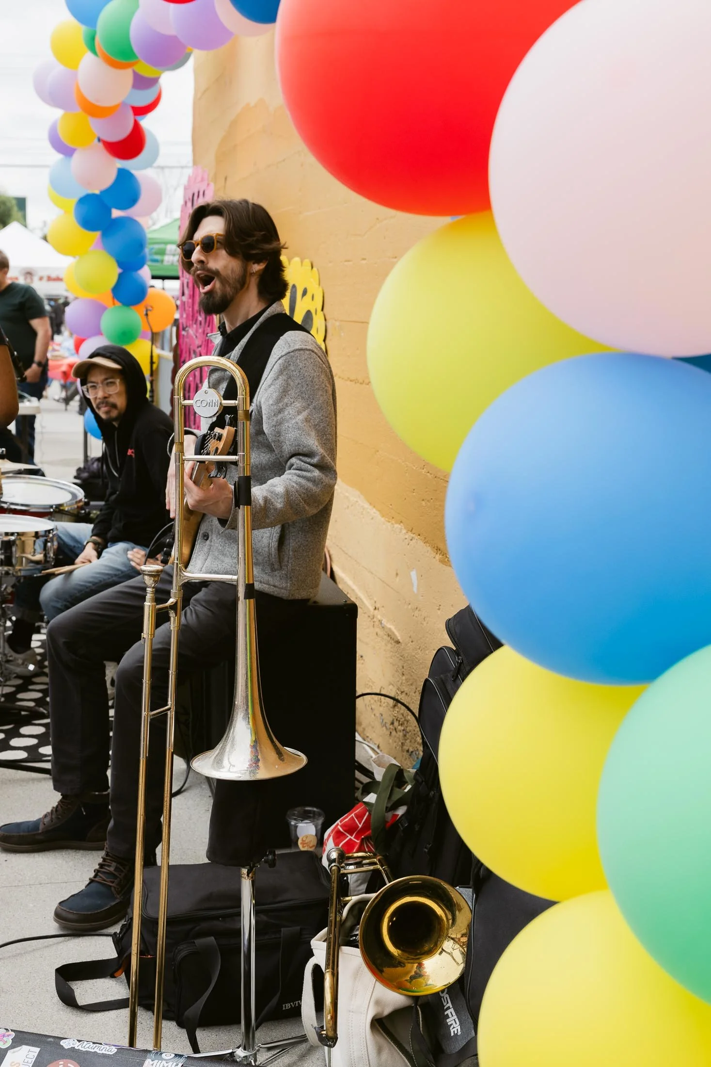 A street musician playing a trumpet at a festival, surrounded by colorful balloons.