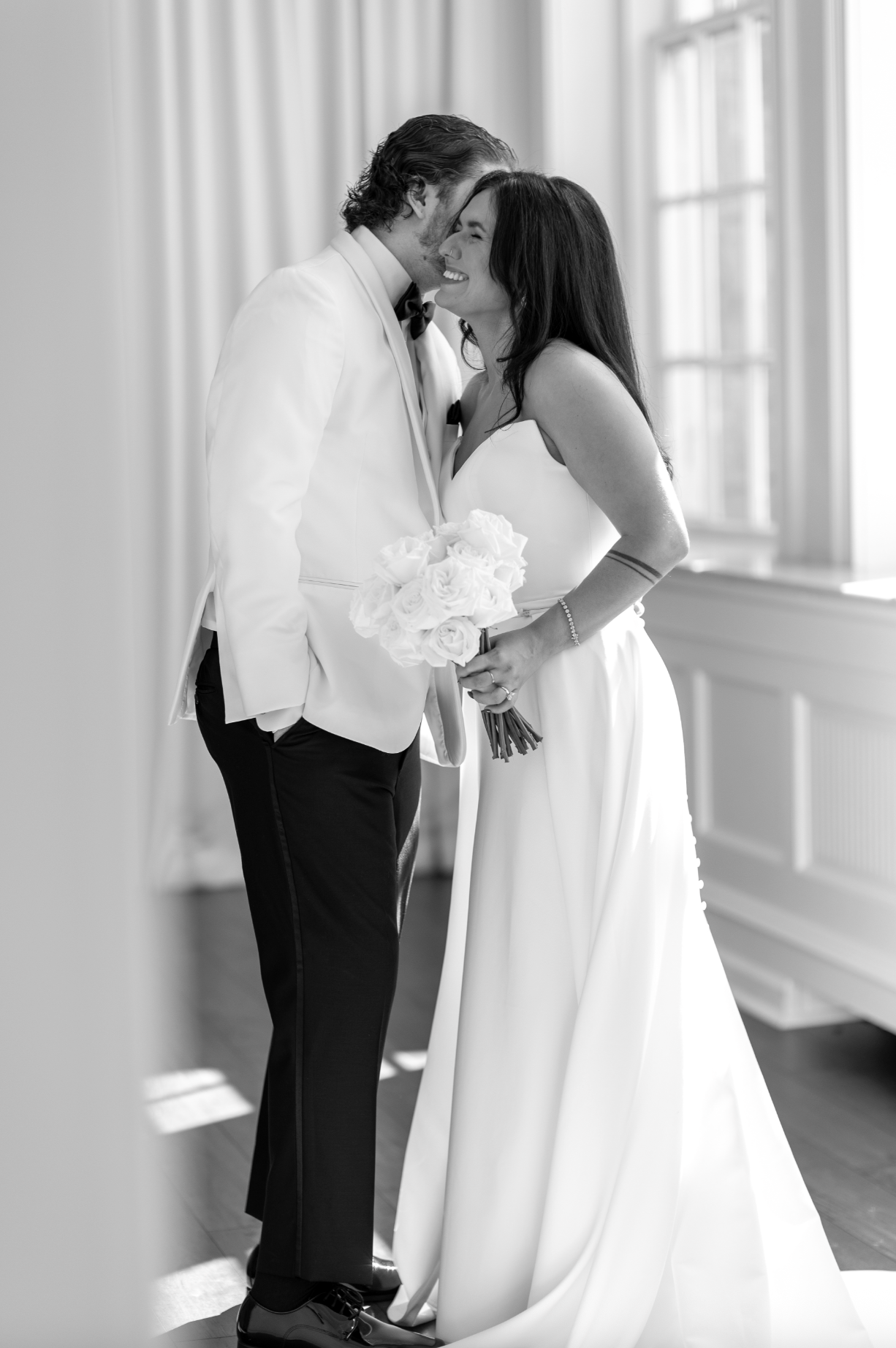Black and white photo of a bride and groom smiling and leaning their foreheads together, with the bride holding a bouquet of white roses. jersey shore wedding photography