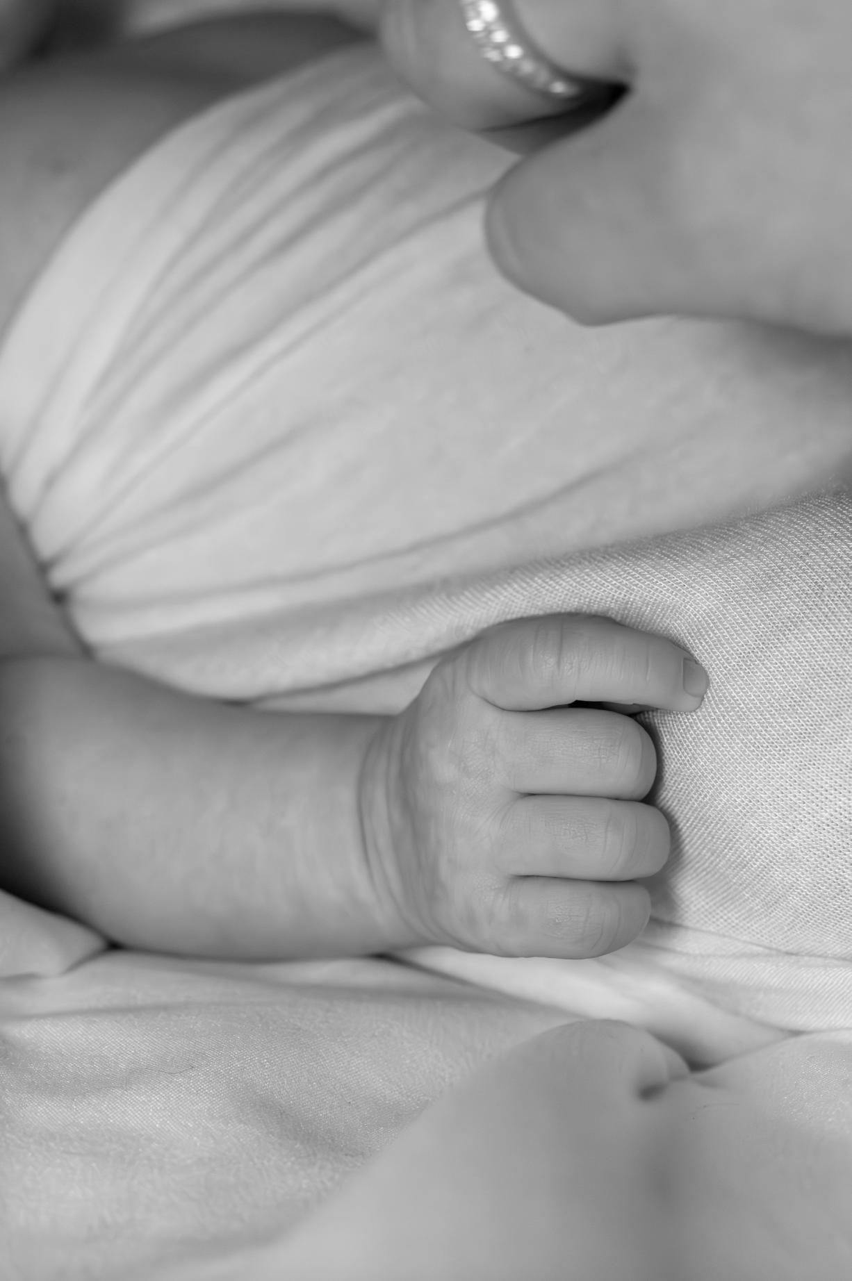 Close-up of a baby's chubby hand resting on fabric, with part of the arm and torso visible, in black and white. jersey shore newborn photography