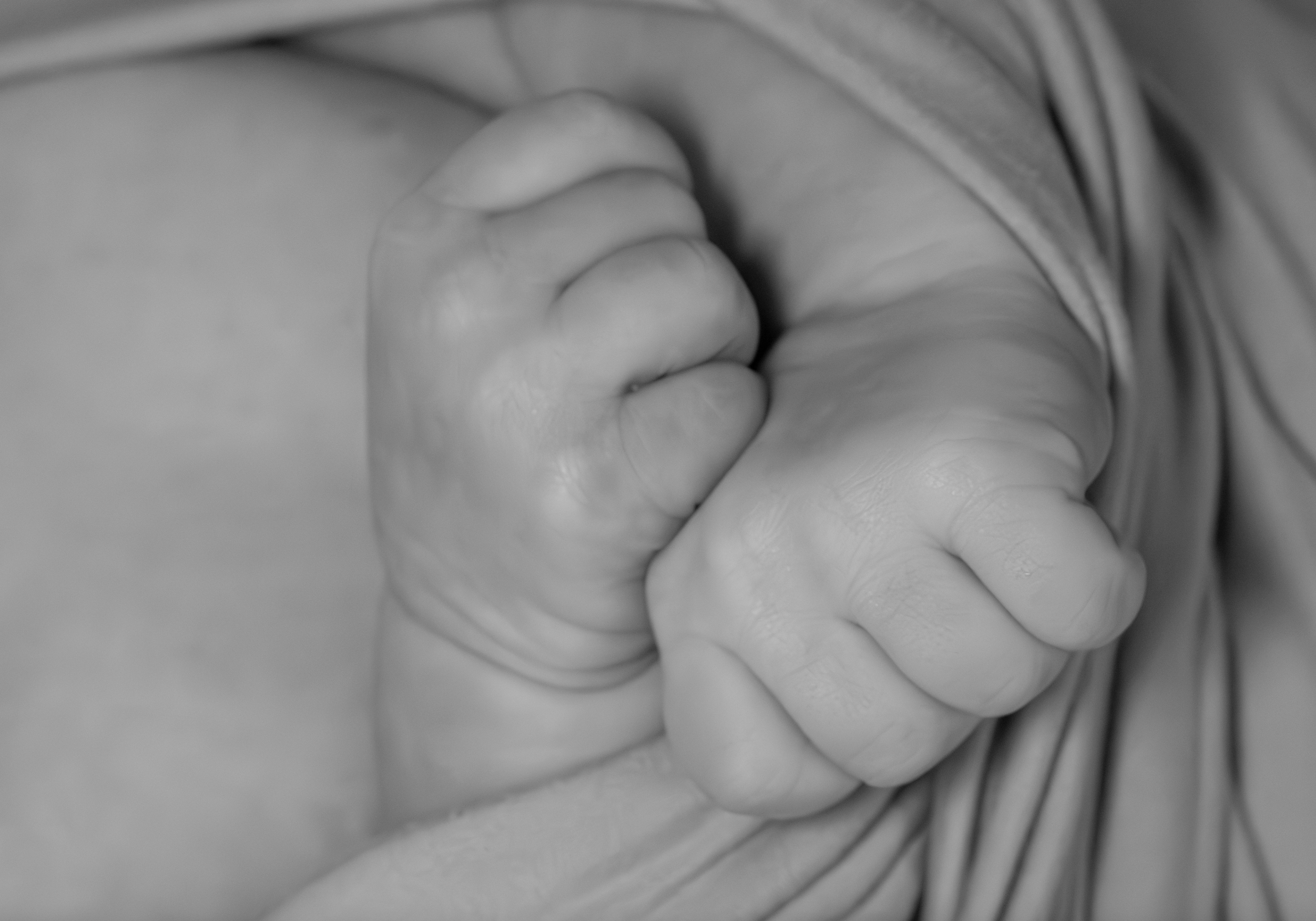 Close-up of a baby's hand curled into a fist, resting on a fabric surface.