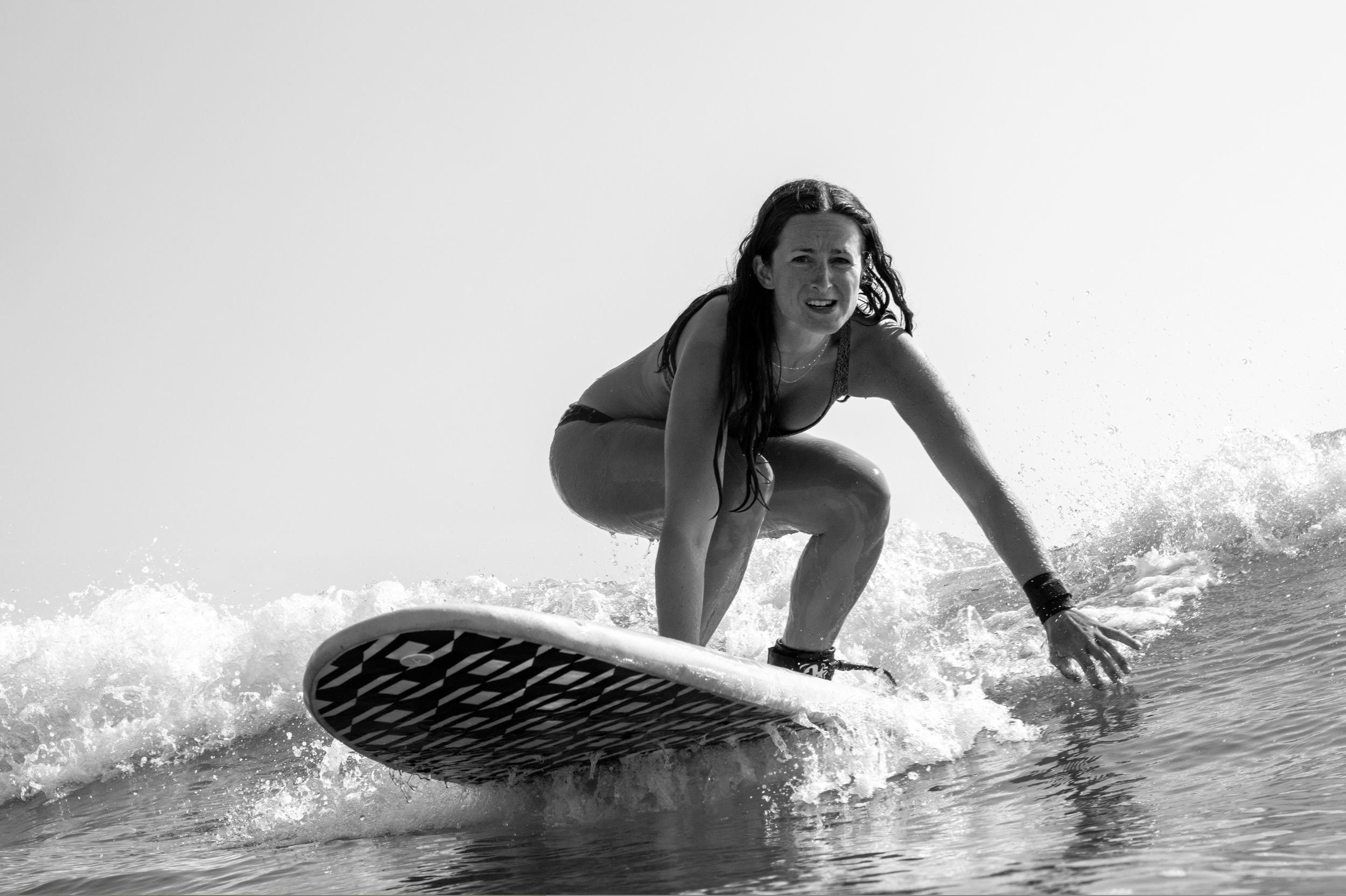 A woman with long dark hair surfing on a wave in the ocean, squatting on her surfboard with a surprised or excited expression. Lavallette, New Jersey Surfer