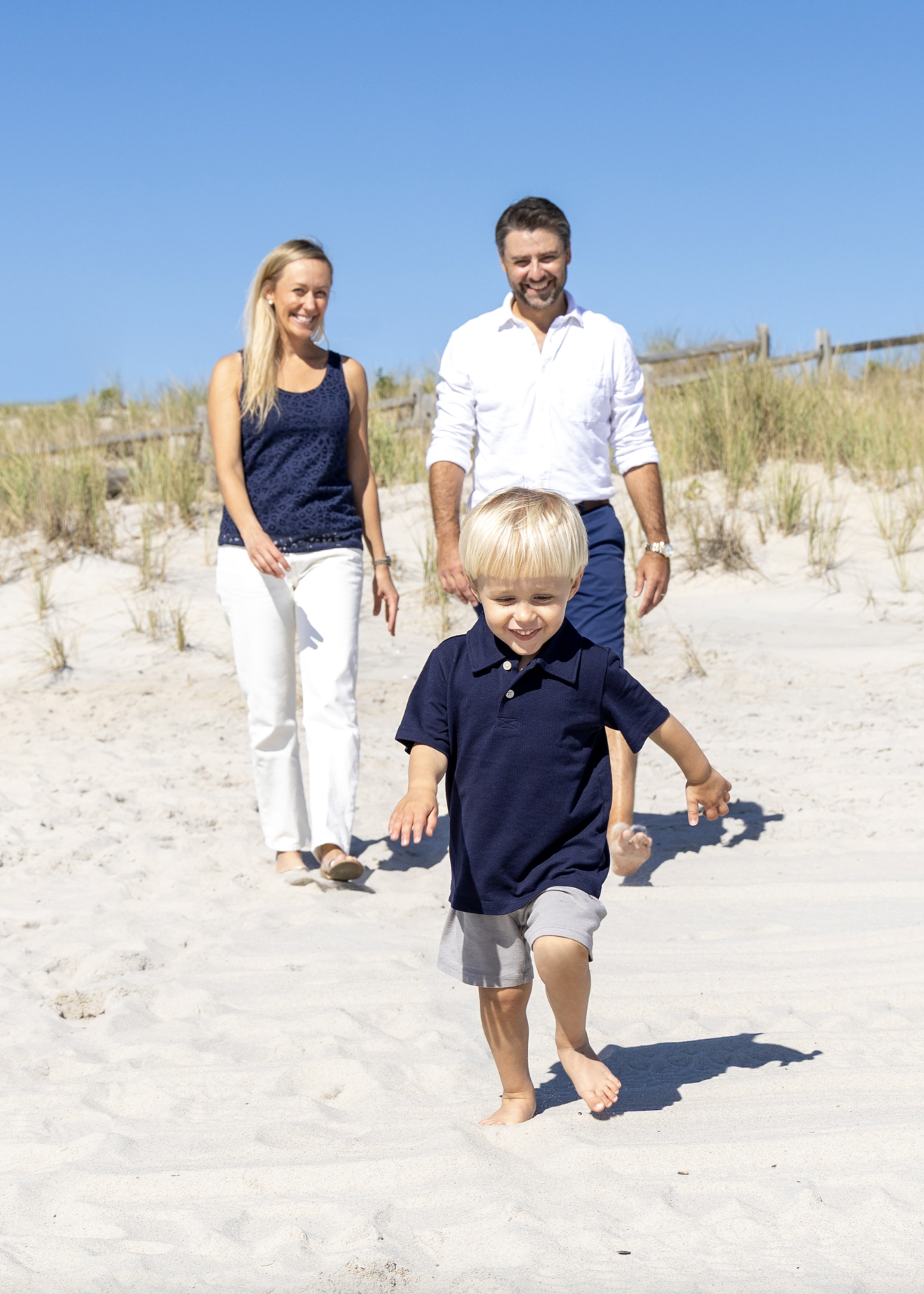A family of three adults and a child walking on a sandy beach on a sunny day with a clear blue sky. Ocean County, New Jersey Family Photographer