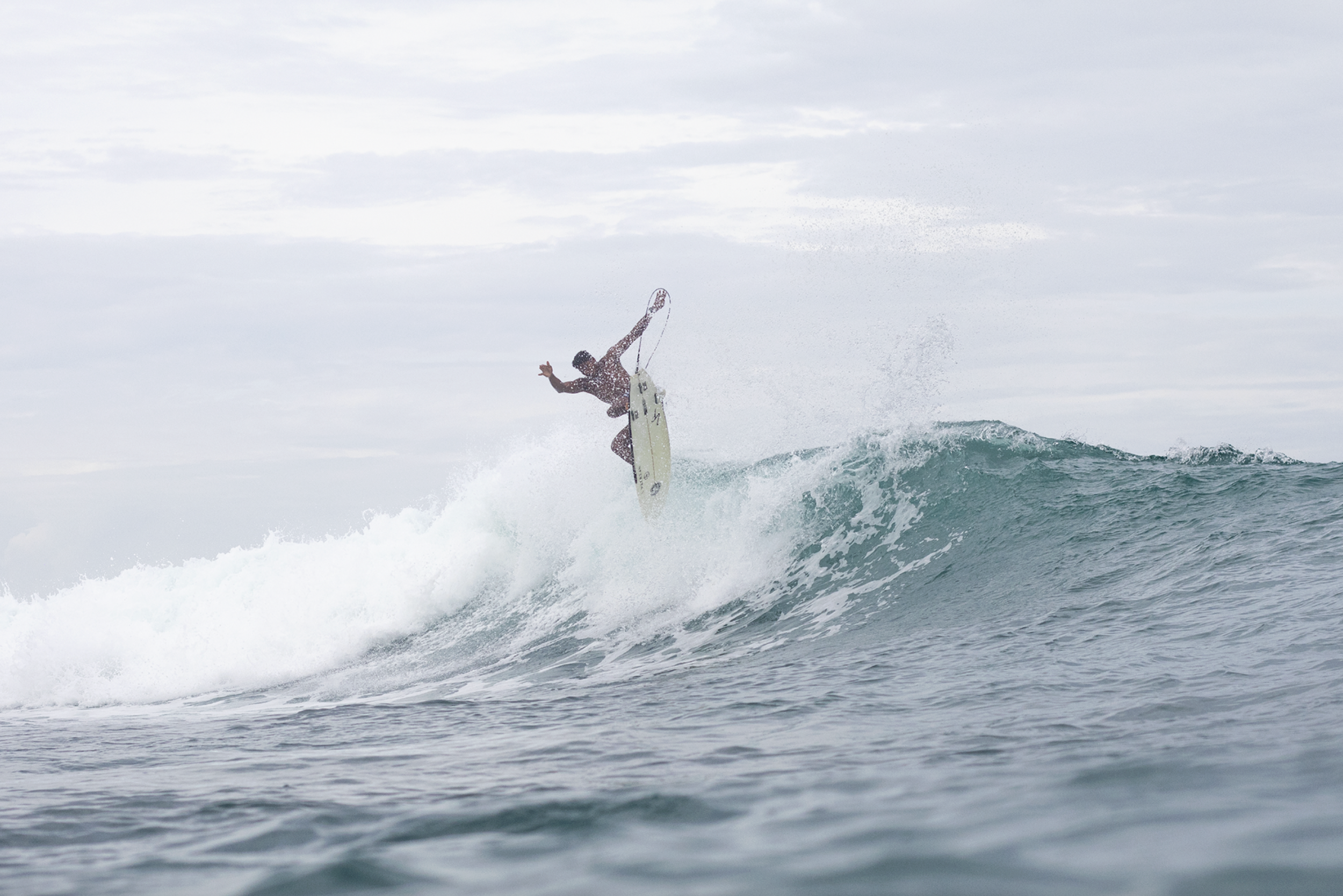 A person surfing on a wave in the ocean under a cloudy sky.