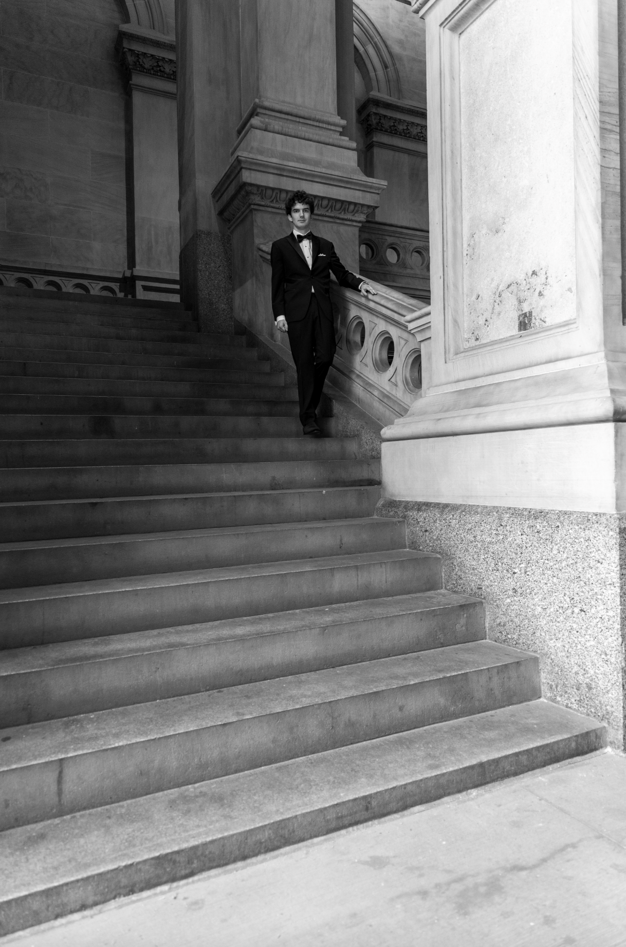 A man in a tuxedo descending a staircase inside a grand, historic building with ornate architectural details.