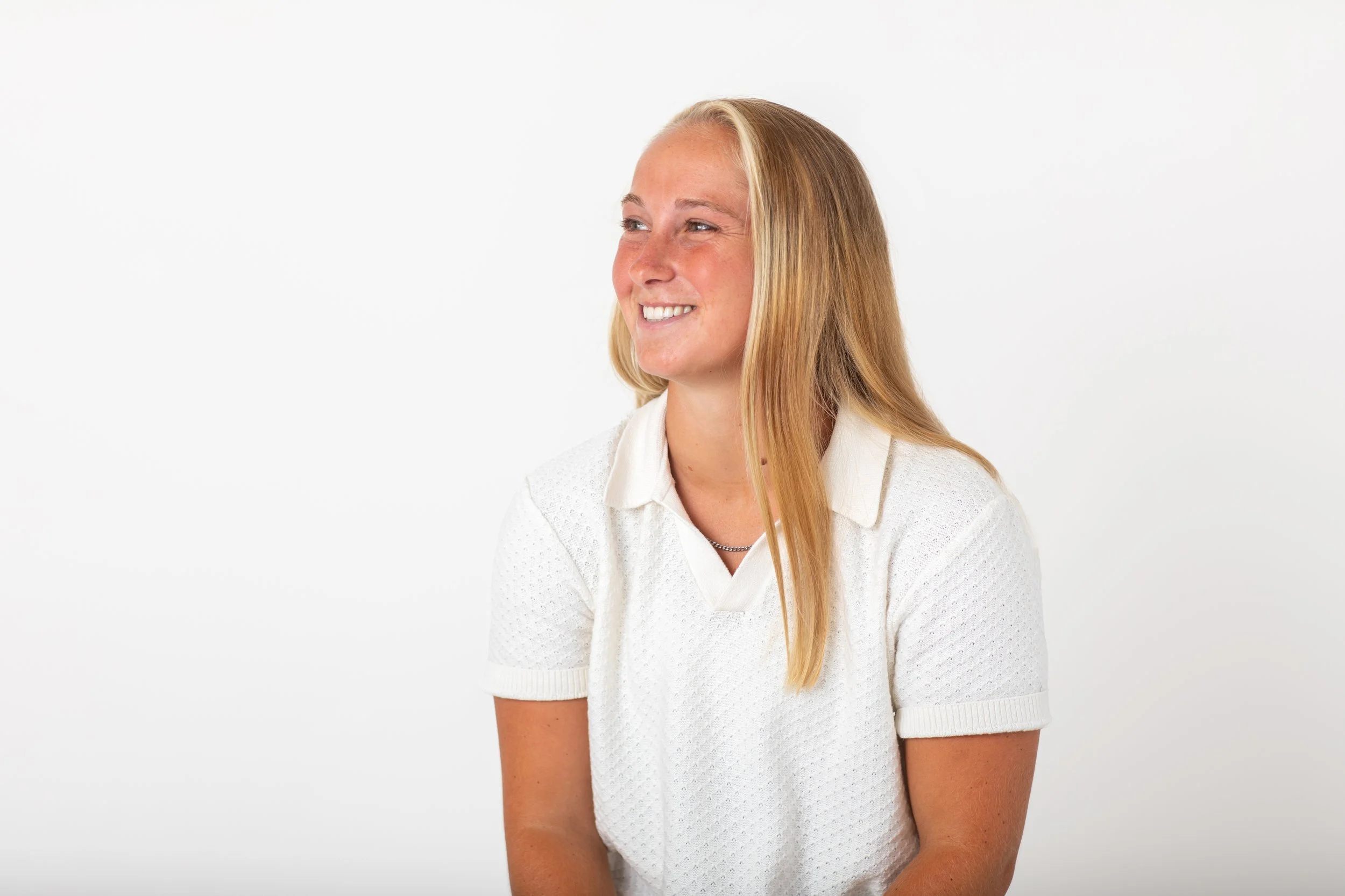 A young woman with blonde hair, wearing a white short-sleeved shirt, smiling and looking slightly to her left against a plain white background. Nicole Burney, Photographer. Lavallette, New Jersey