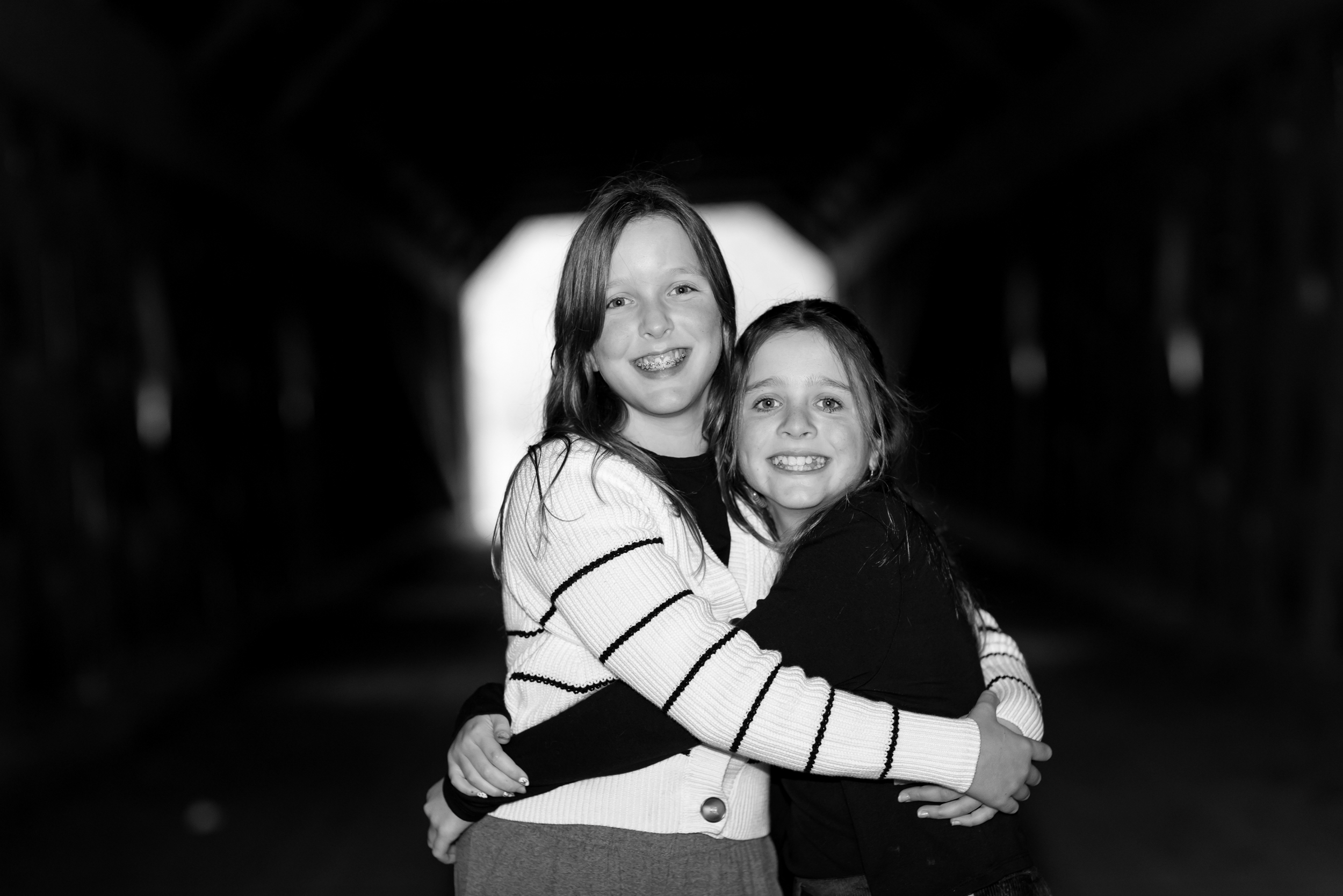 Two young girls hugging and smiling in a tunnel, in black and white.