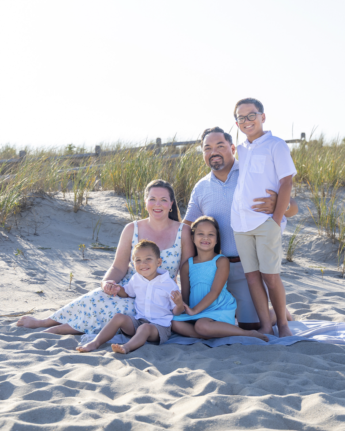 A happy family of six sitting on the sand at the beach, smiling and posing for the photo. Monmouth County, New jersey beach family photos