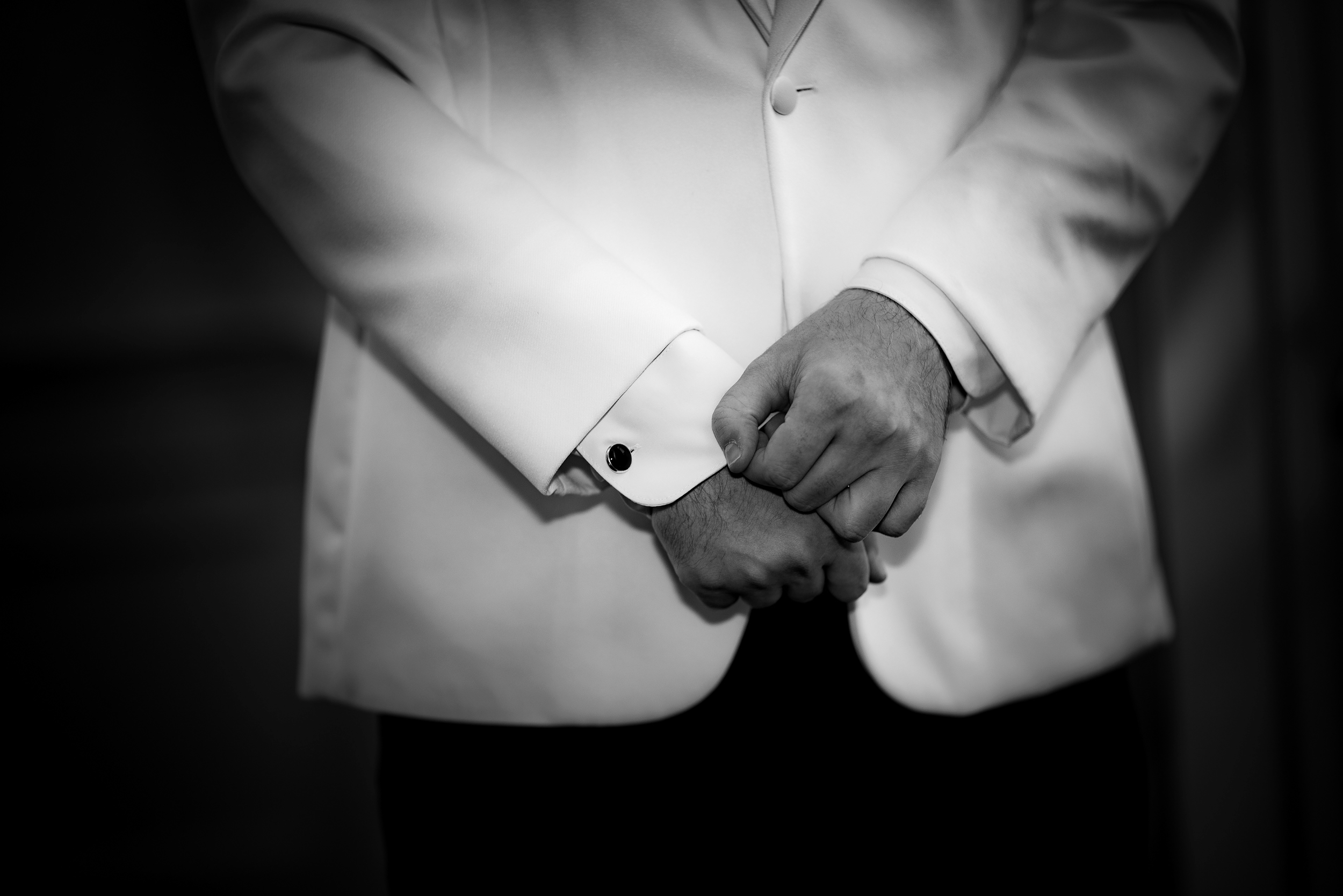 Black and white photo of a man adjusting his cufflinks on a formal shirt, focusing on his hands and sleeves.