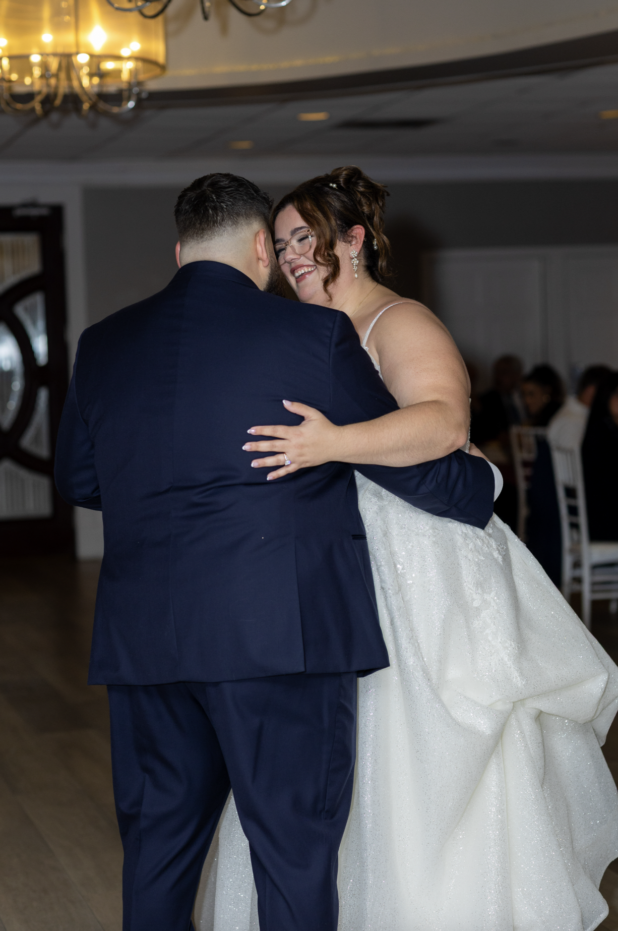 A bride and groom dancing at their wedding reception, smiling and embracing each other.