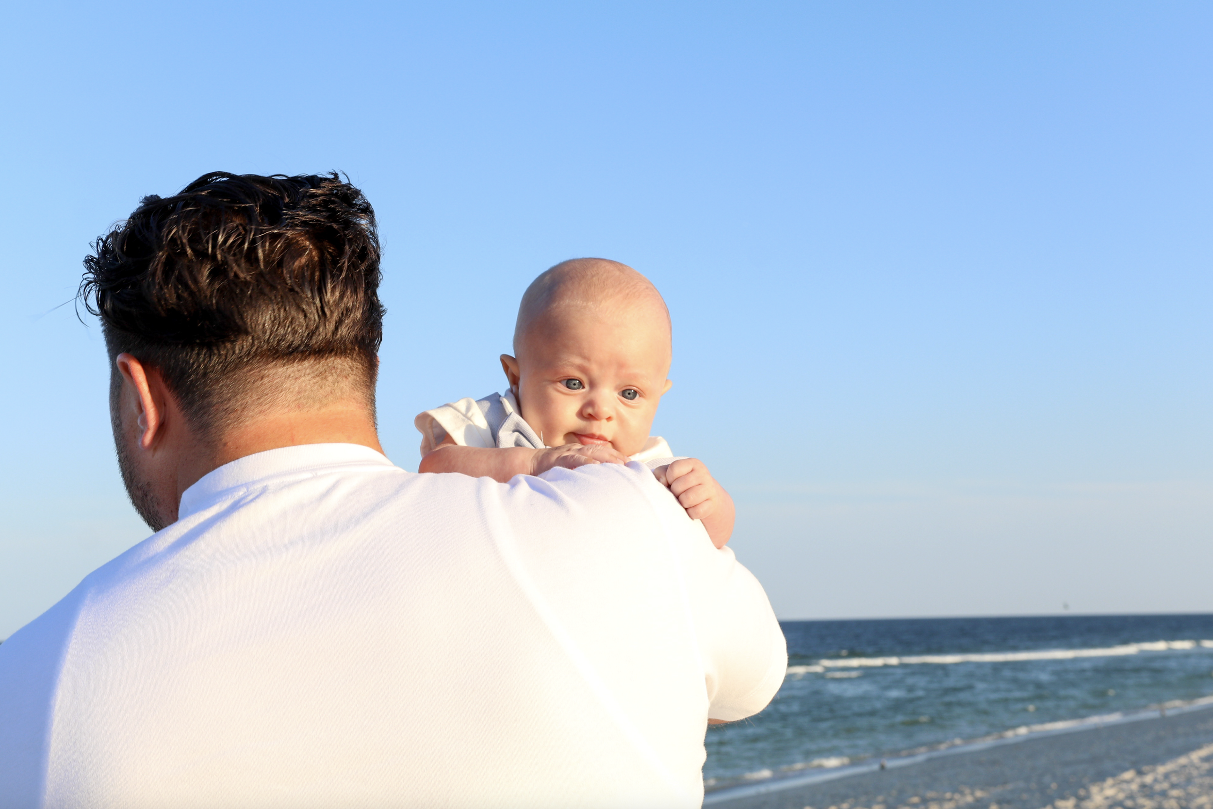 A man holding a baby on a beach with the ocean in the background.
