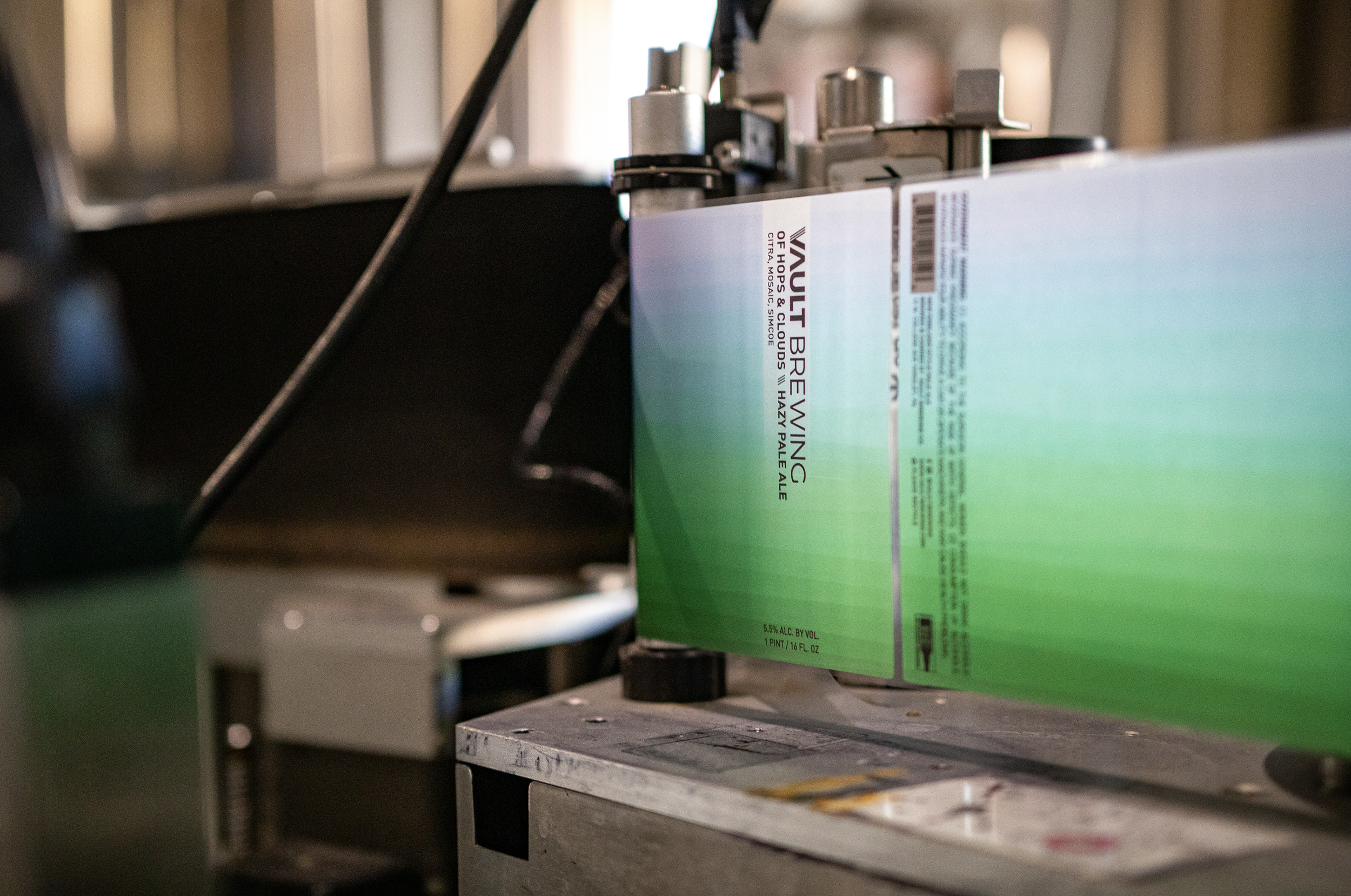 A close-up of a large green and white cardboard box with a barcode and label, on machinery in a factory or manufacturing setting. Vault Brewing, Yardley, PA Headshot session