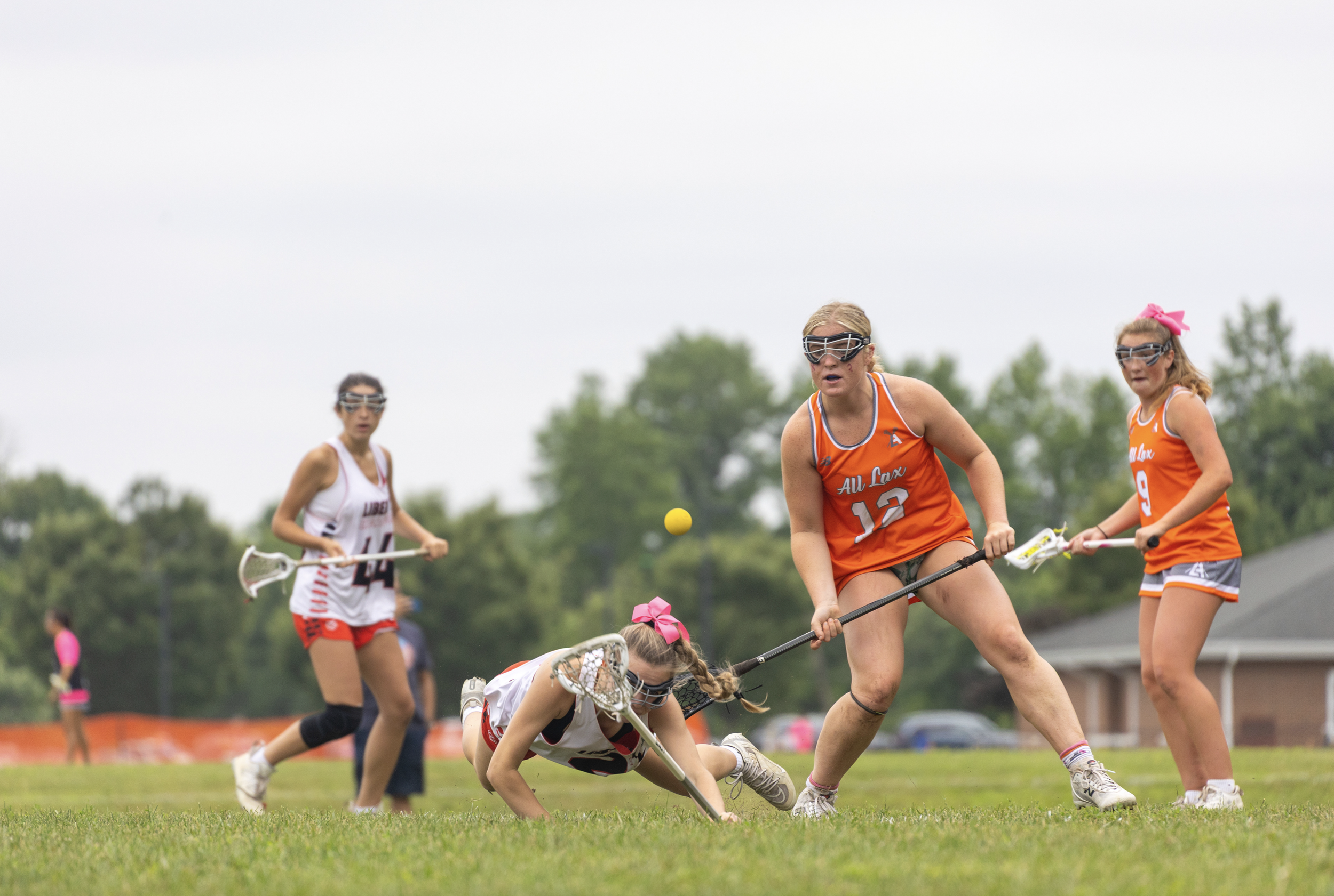Lacrosse players in action on a field, with one player falling to the ground while others stand and play.
