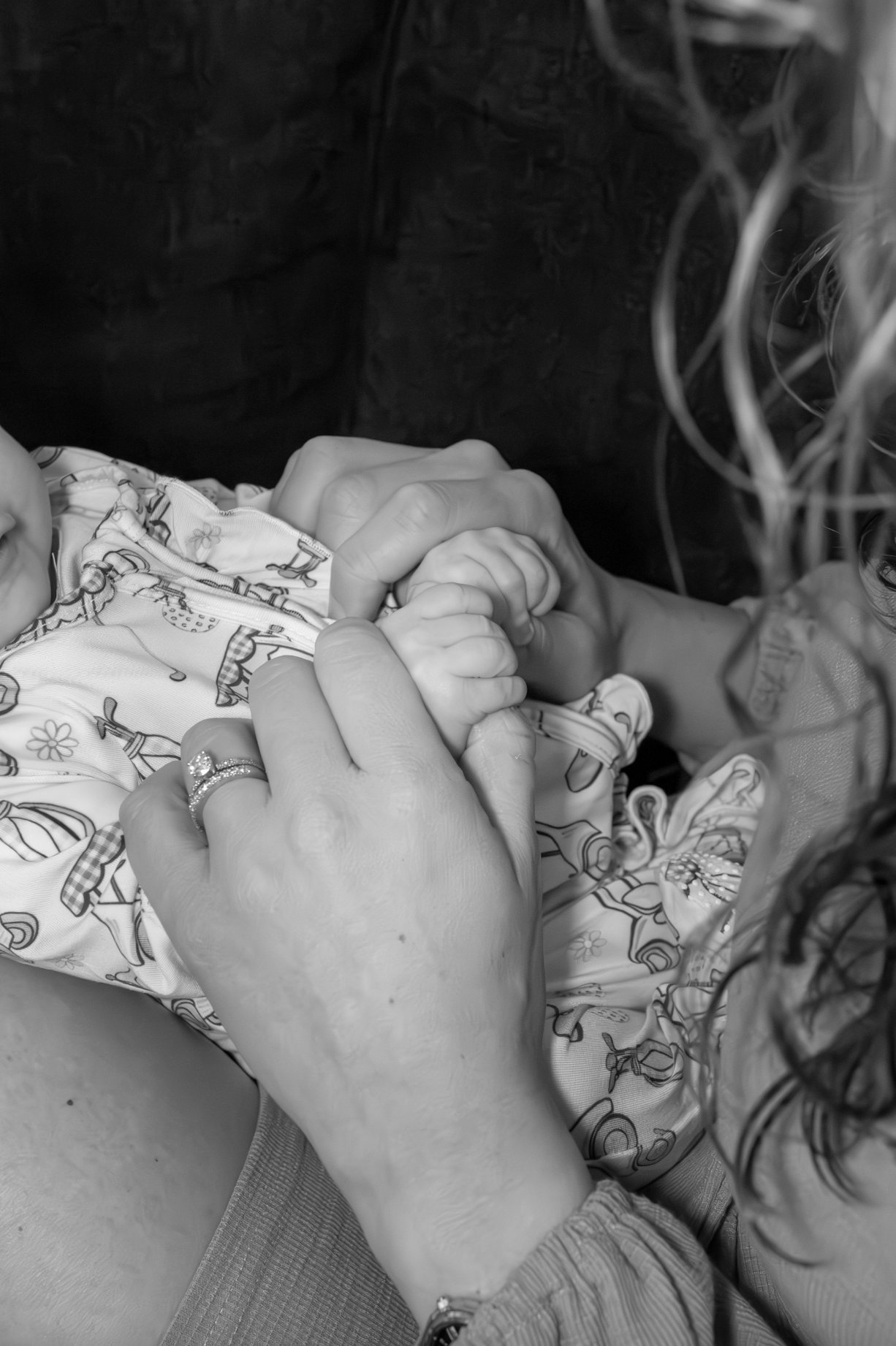 Close-up of an adult holding a baby's hand, both hands interlocked, with a ring visible on the adult's finger, in a tender moment. Jersey Shore newborn photography