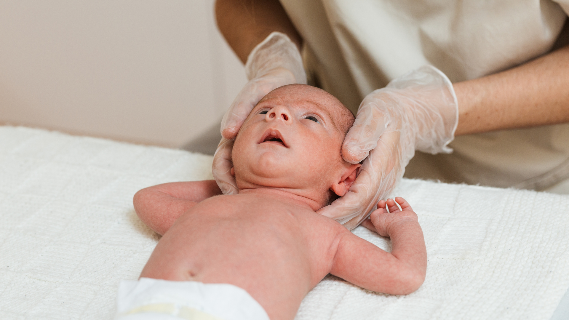 Un bébé allongé sur une table, ayant le visage orienté vers le haut, pendant qu'une personne portant des gants examine son visage.