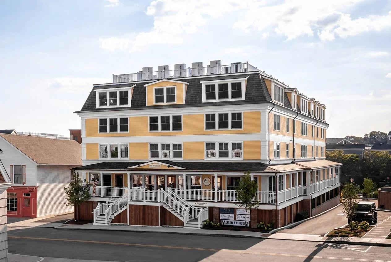 A four-story mixed-use building with a yellow and white exterior, large windows, a wrap-around porch on the second and third floors, an entrance with stairs, and surrounding parking lot.