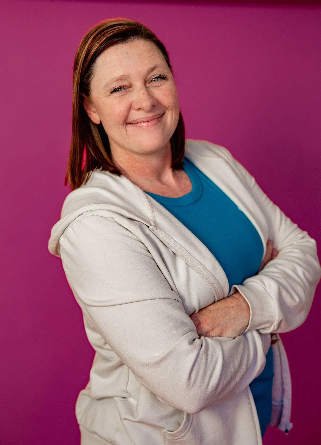 Liz Chapman, podcast manager and launch coach, smiling at the camera with her arms crossed against a bright pink background