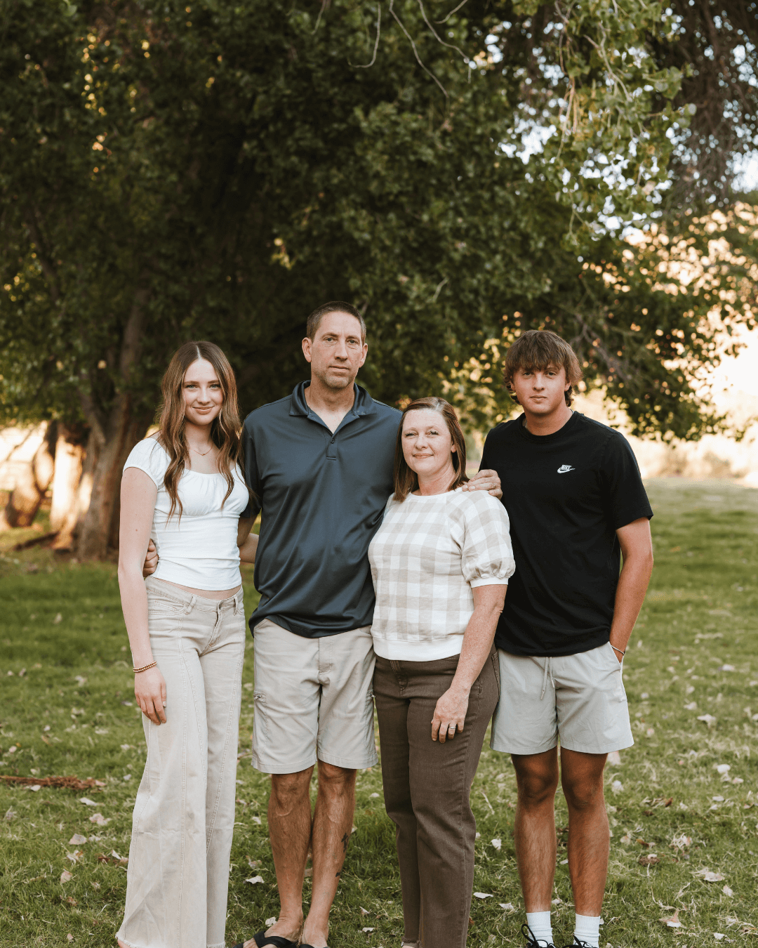 A family photo of Liz, Ryan, Madi and Cooper standing outside in a pasture with trees behind them at golden hour